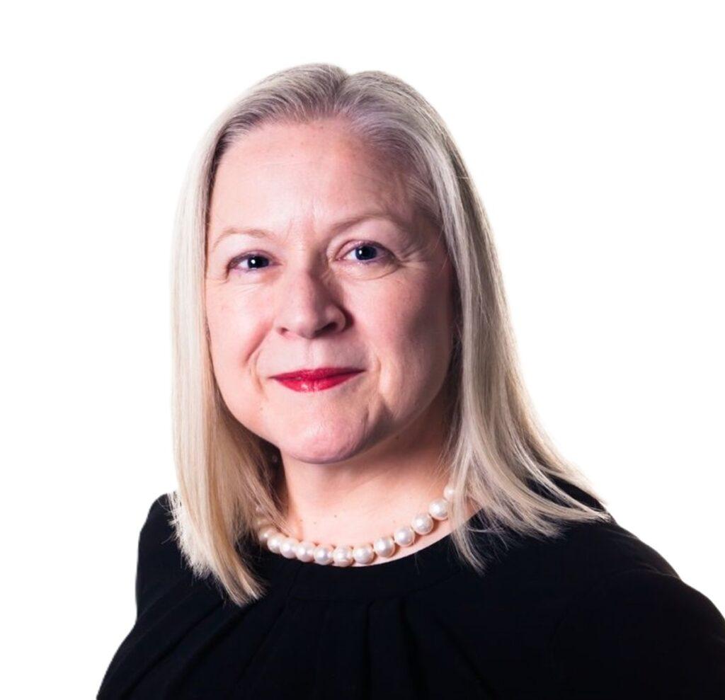 Portrait of Cath Hill, CEO of Gem-A, wearing a black top and pearl necklace against a neutral background.