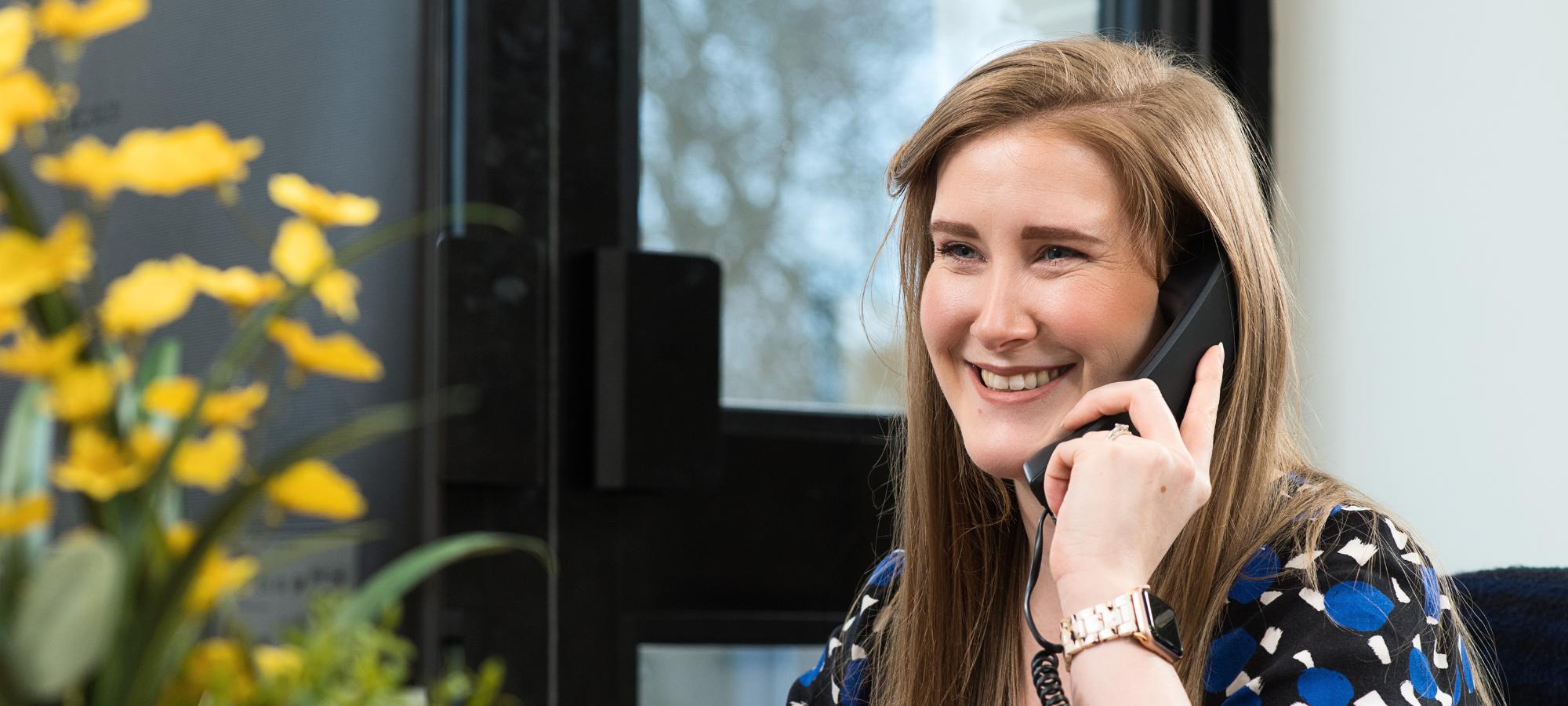 A smiling Weston Beamor team member speaks with a customer by telephone from her desk.