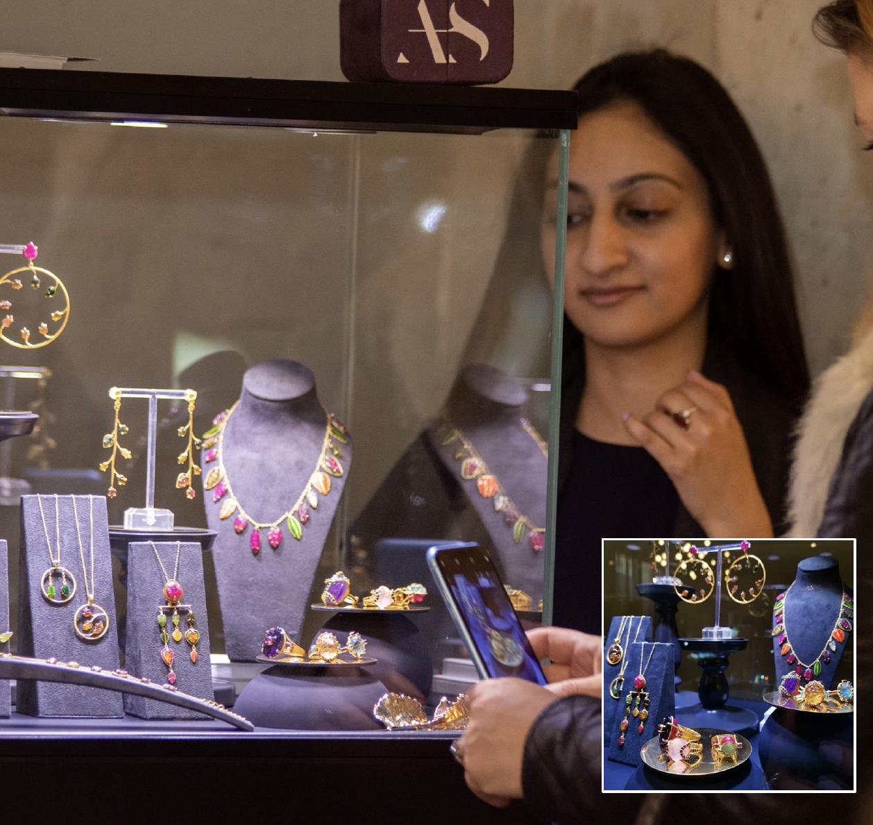 Jewellery designer Akansha Sethi standing beside an illuminated glass showcase filled with colourful necklaces, earrings and rings at The Jewellery Cut Live