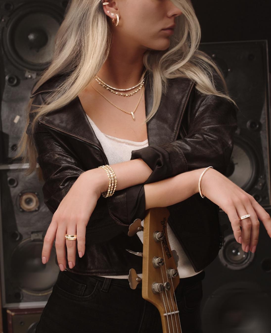 Model wearing Pragnell RockChic diamond bracelets, rings and layered gold necklaces, styled with a leather jacket against a speaker backdrop.