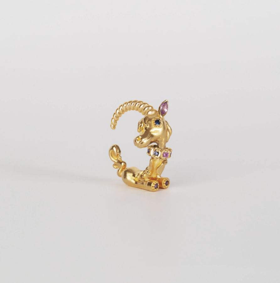 Small gold unicorn jewel standing upright on a white background, with a curled horn and pink, blue and clear gemstone accents.