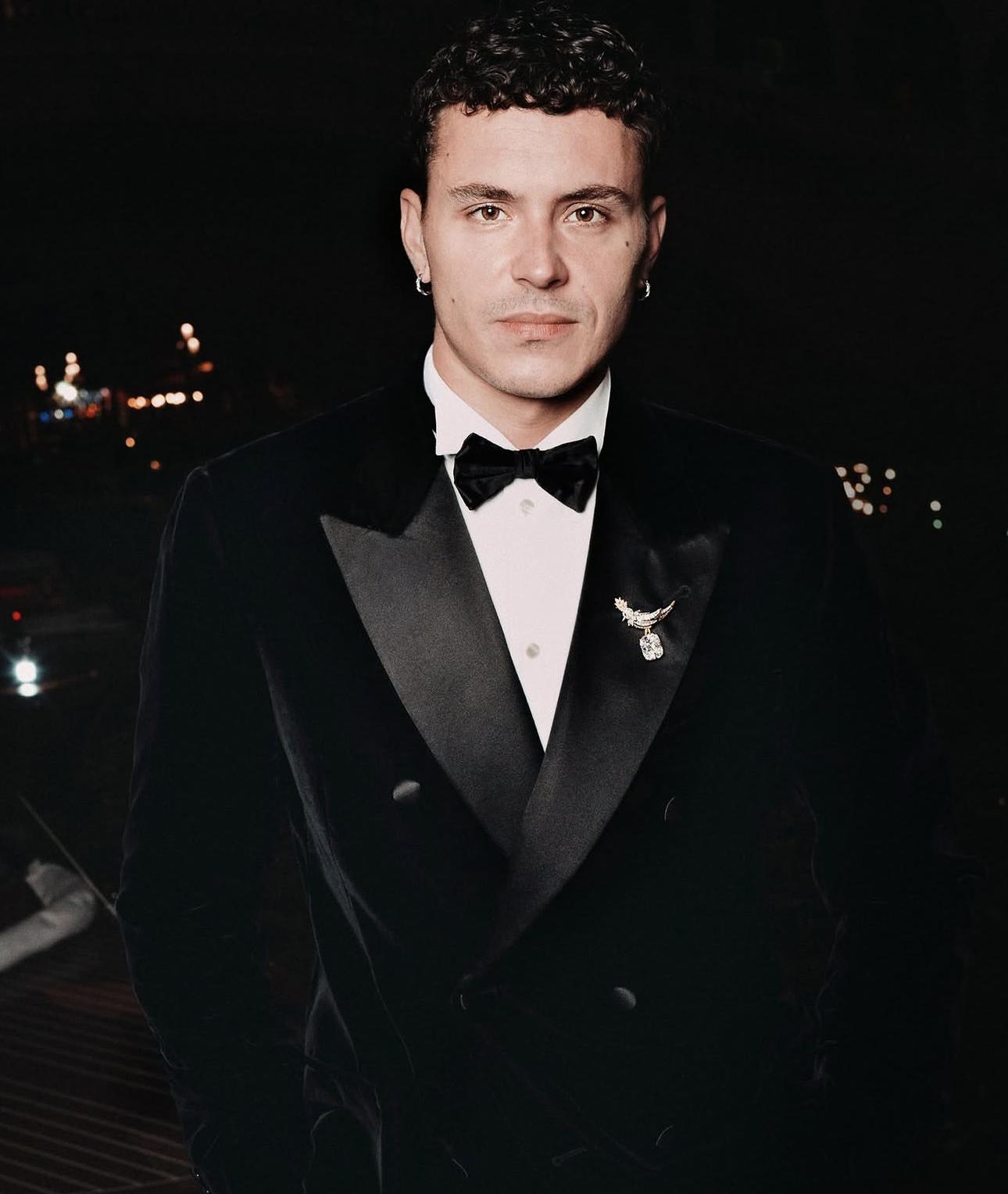 Arón Piper in a black velvet tuxedo wearing a winged Tiffany brooch on his lapel and a diamond-set watch