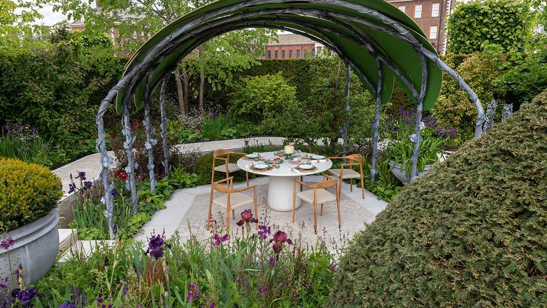 The Boodles Garden at RHS Chelsea Flower Show featuring a curved garden structure, landscaped planting and outdoor dining area surrounded by flowers and greenery.