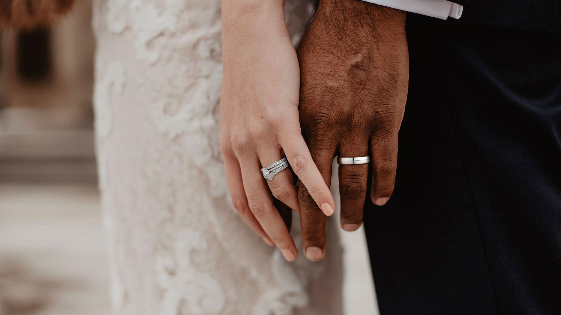 Close-up of a couple holding hands, wearing diamond engagement rings and plain wedding bands.