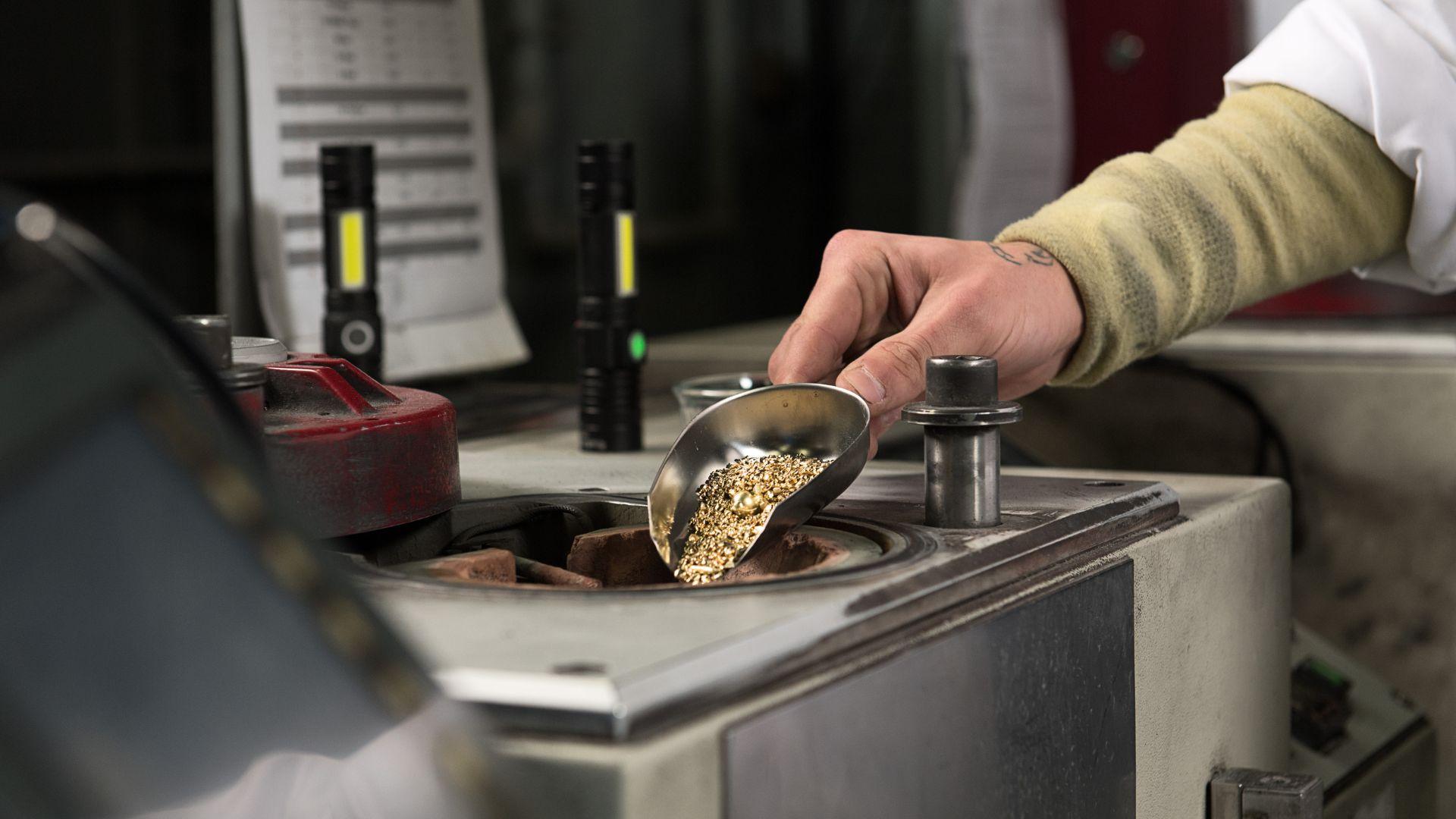 Craftsperson pouring gold coloured metal granules into a melting furnace in a jewellery workshop.