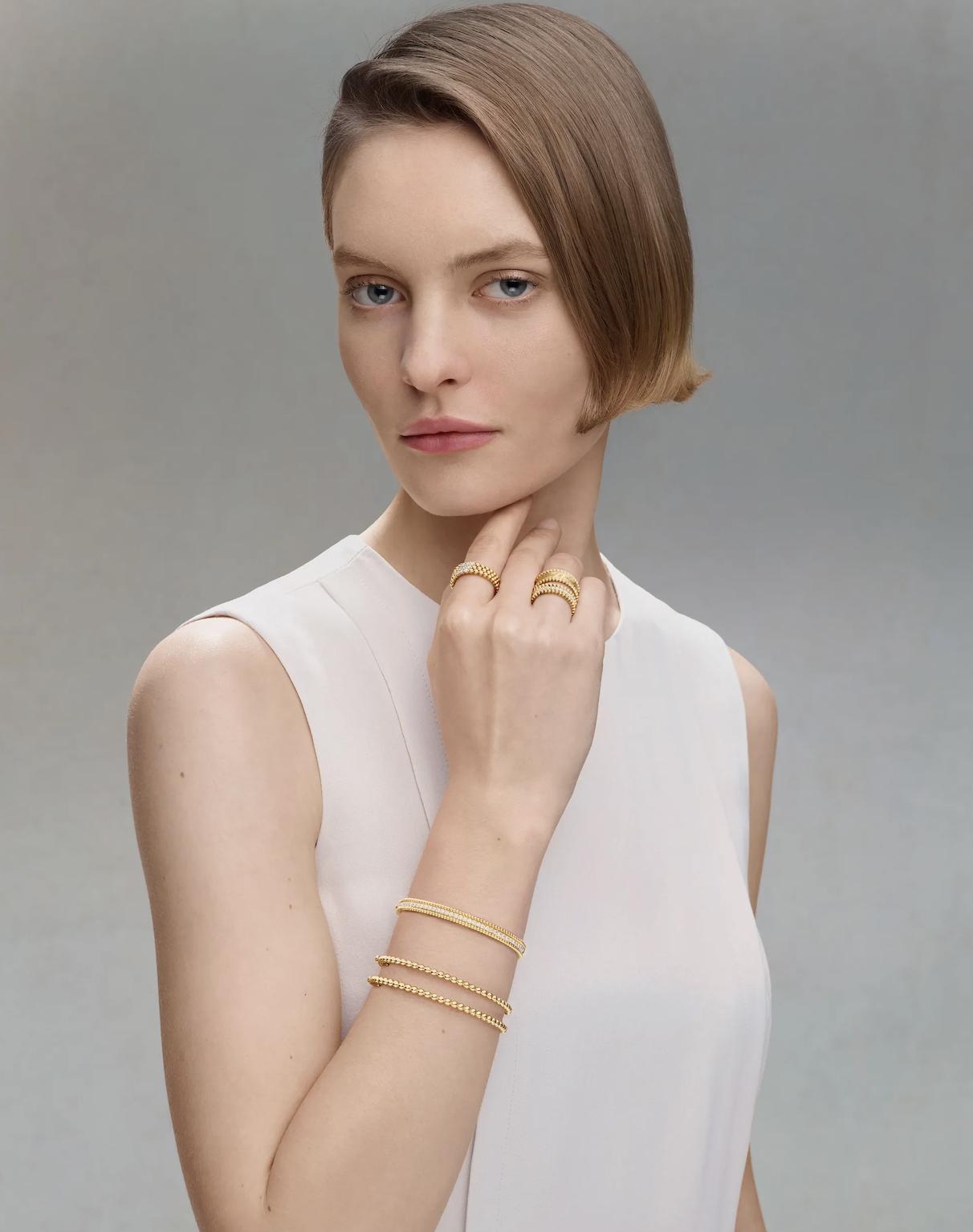 Model wearing multiple Van Cleef & Arpels Perlée yellow gold and diamond rings styled across both hands against a neutral studio background.