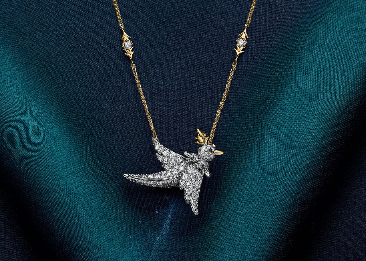 Tiffany & Co. Bird on a Rock necklace featuring a diamond-set bird with gold accents, focusing on wing detail against a dark fabric background.