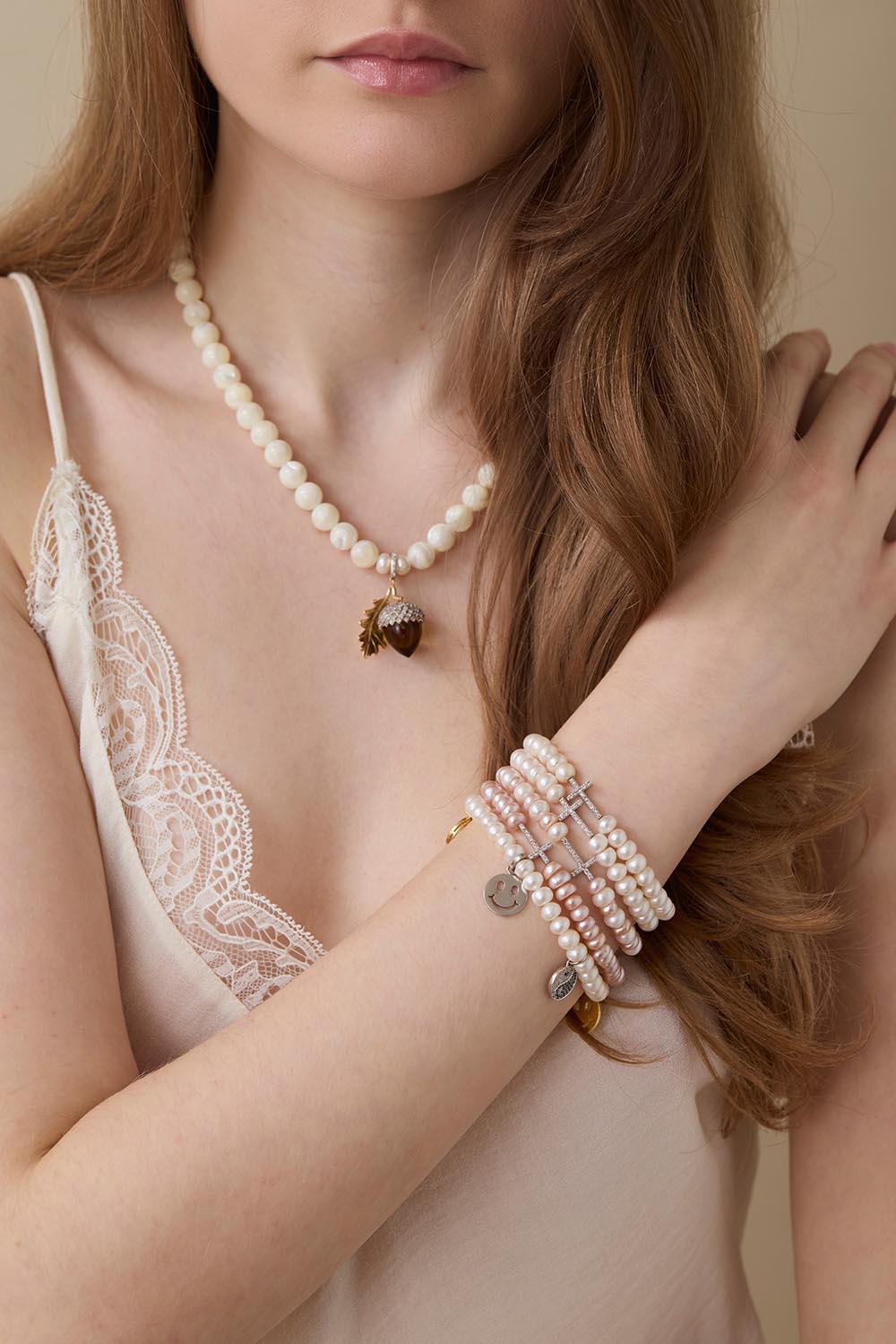 Model wearing a pearl necklace with Tash Jewellery’s smoky-quartz and diamond acorn charm, alongside layered pearl charm bracelets