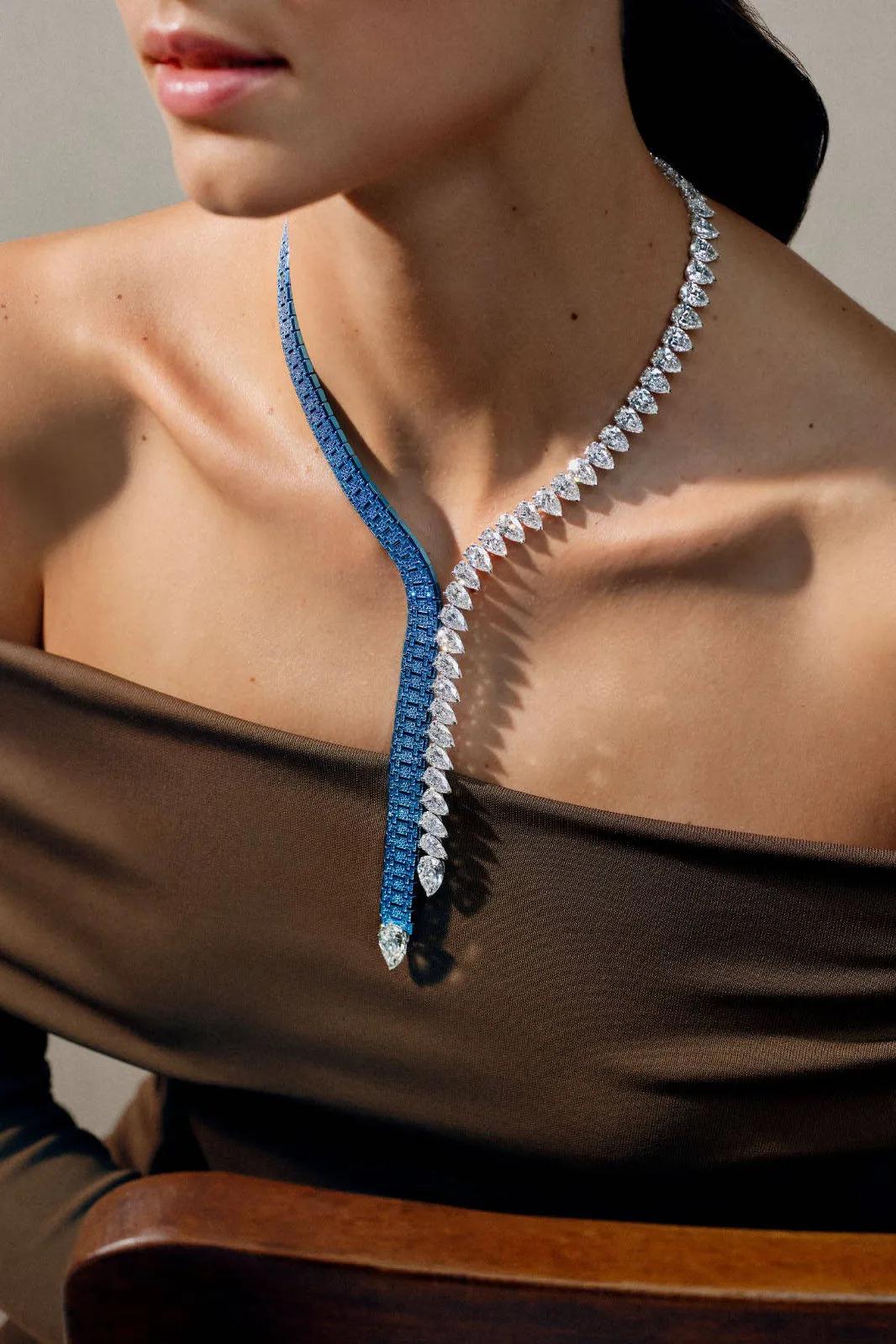 Model wearing an asymmetric Audemars Piguet tie necklace with a blue sapphire-set titanium strand crossing a line of pear-shaped white diamonds.