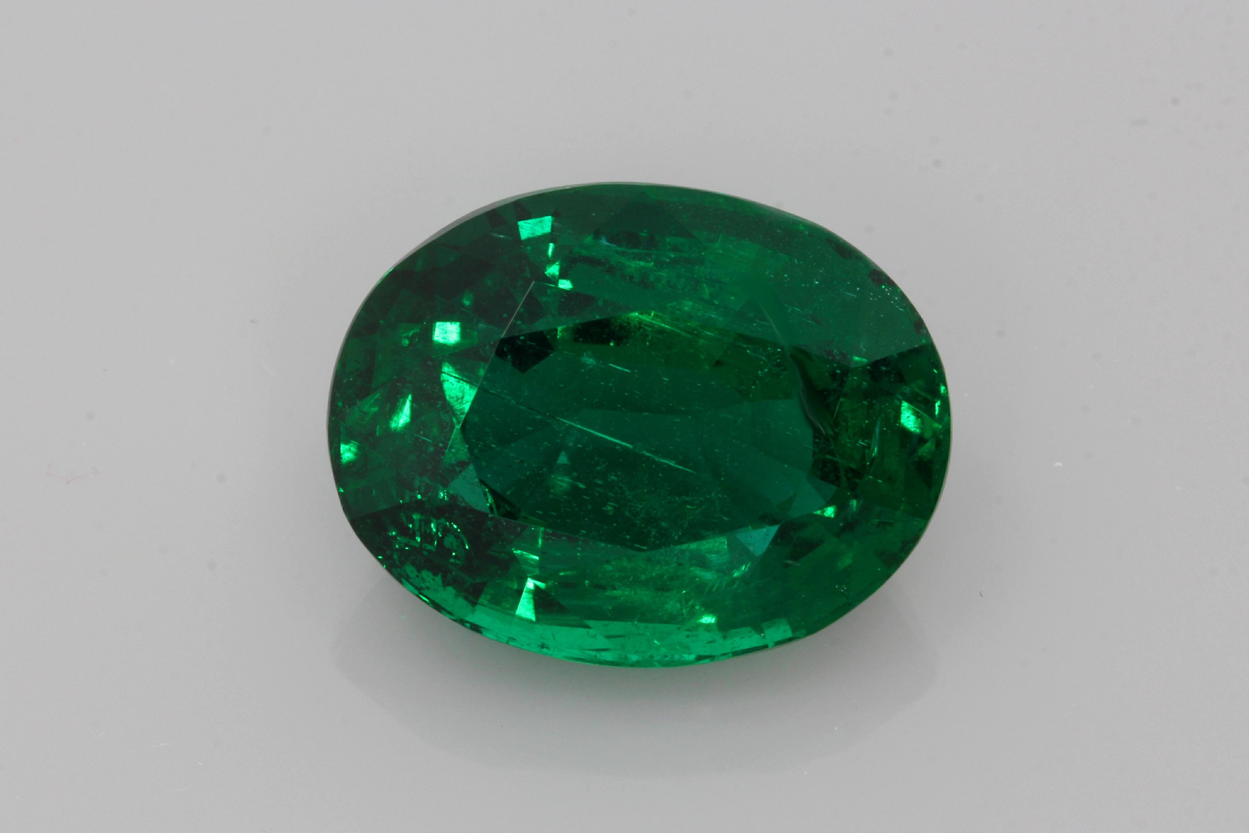 Large oval-cut Zambian emerald with deep green colour photographed against a white background.