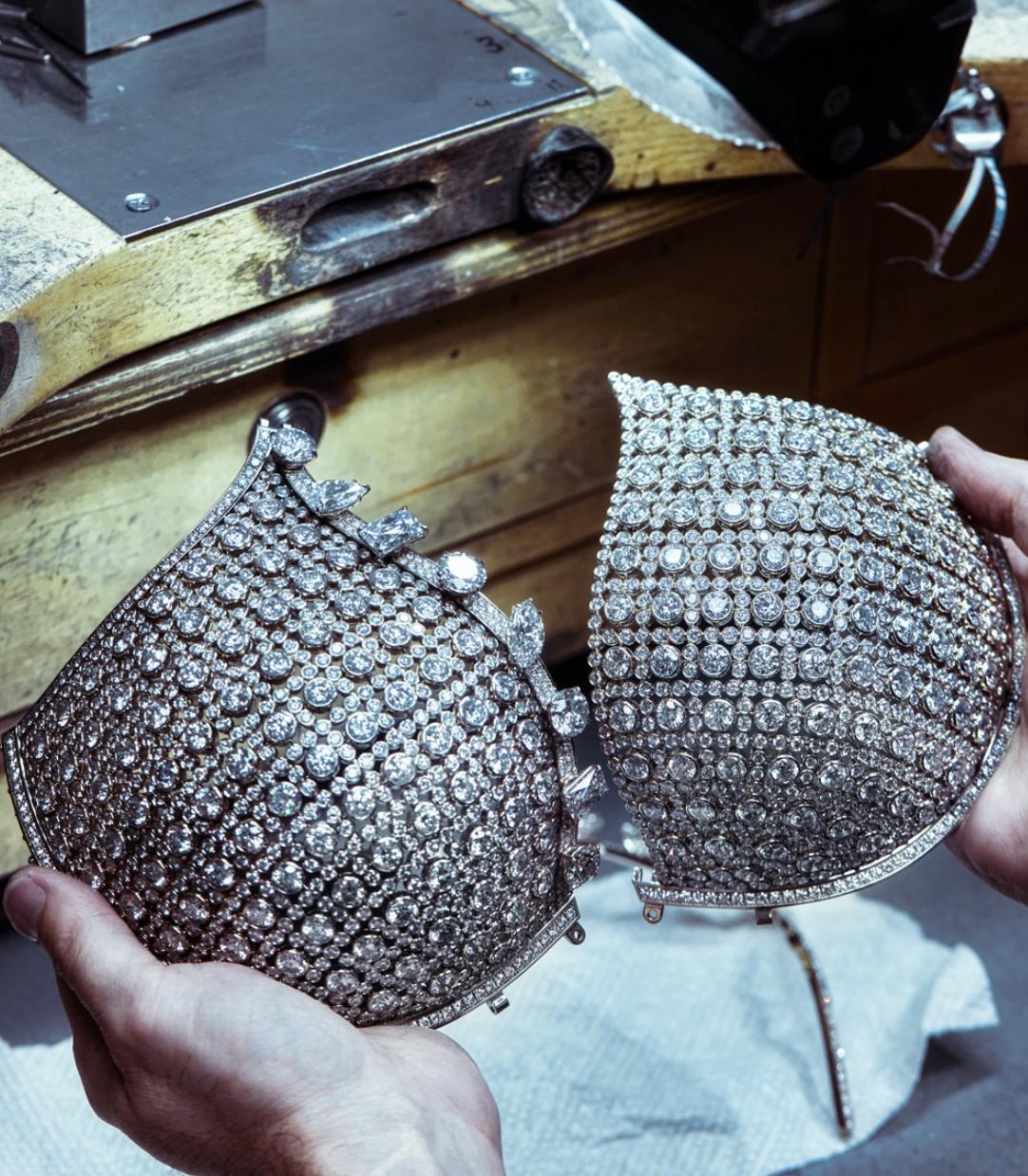 A Jacob & Co. artisan holds the two diamond covered cups of the Angel Fantasy Bra above a jeweller’s workbench during construction