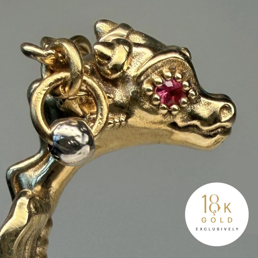 Macro view of an 18-karat gold dragon’s head with a round red ruby eye and a polished silver-toned bead beside its neck.