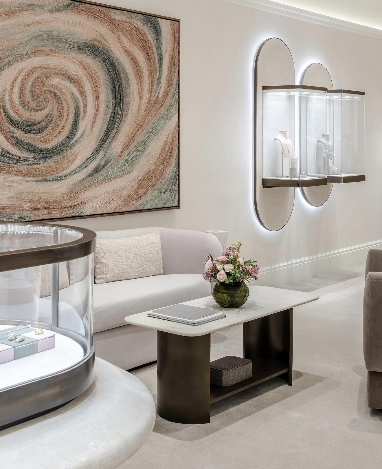 Interior of The Boodles Townhouse with illuminated jewellery cases, a pale sofa, marble-topped table, pink flowers and a large abstract spiral artwork