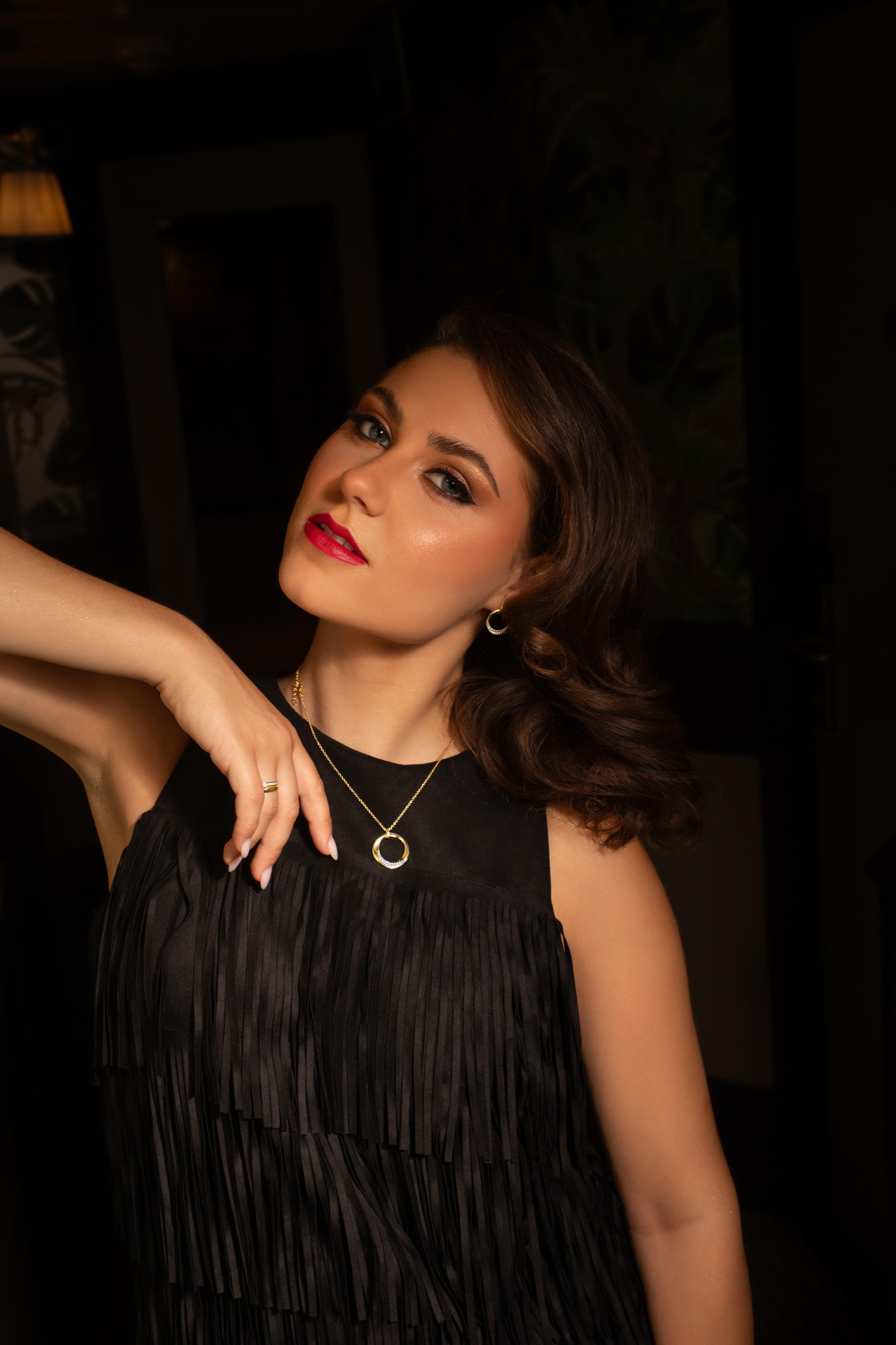 Gisser campaign image featuring a model wearing a gold-plated necklace, hoop earrings and ring with a black fringed dress.