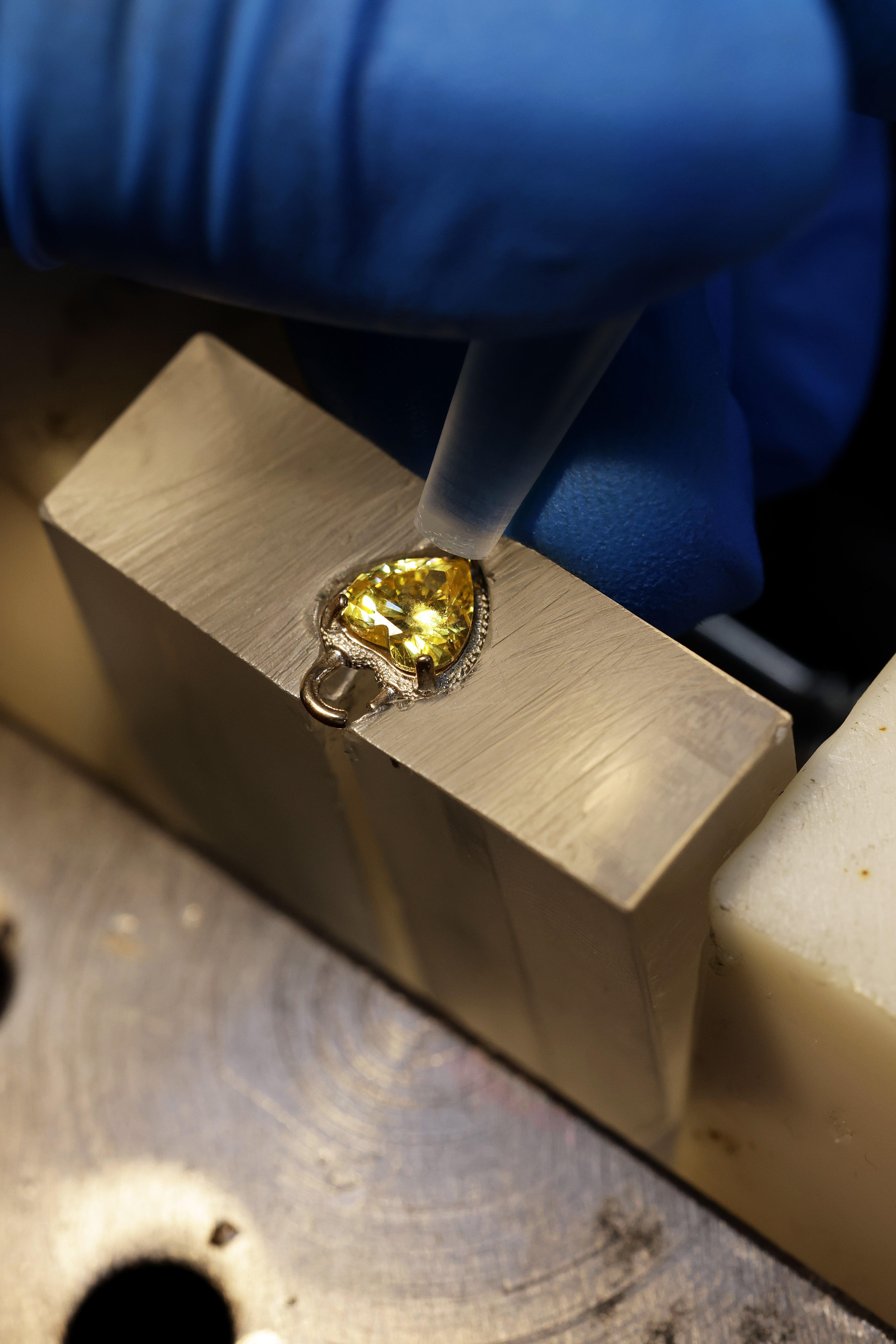 Close-up of a gloved craftsperson securing a pear-cut yellow stone into a metal jewellery setting