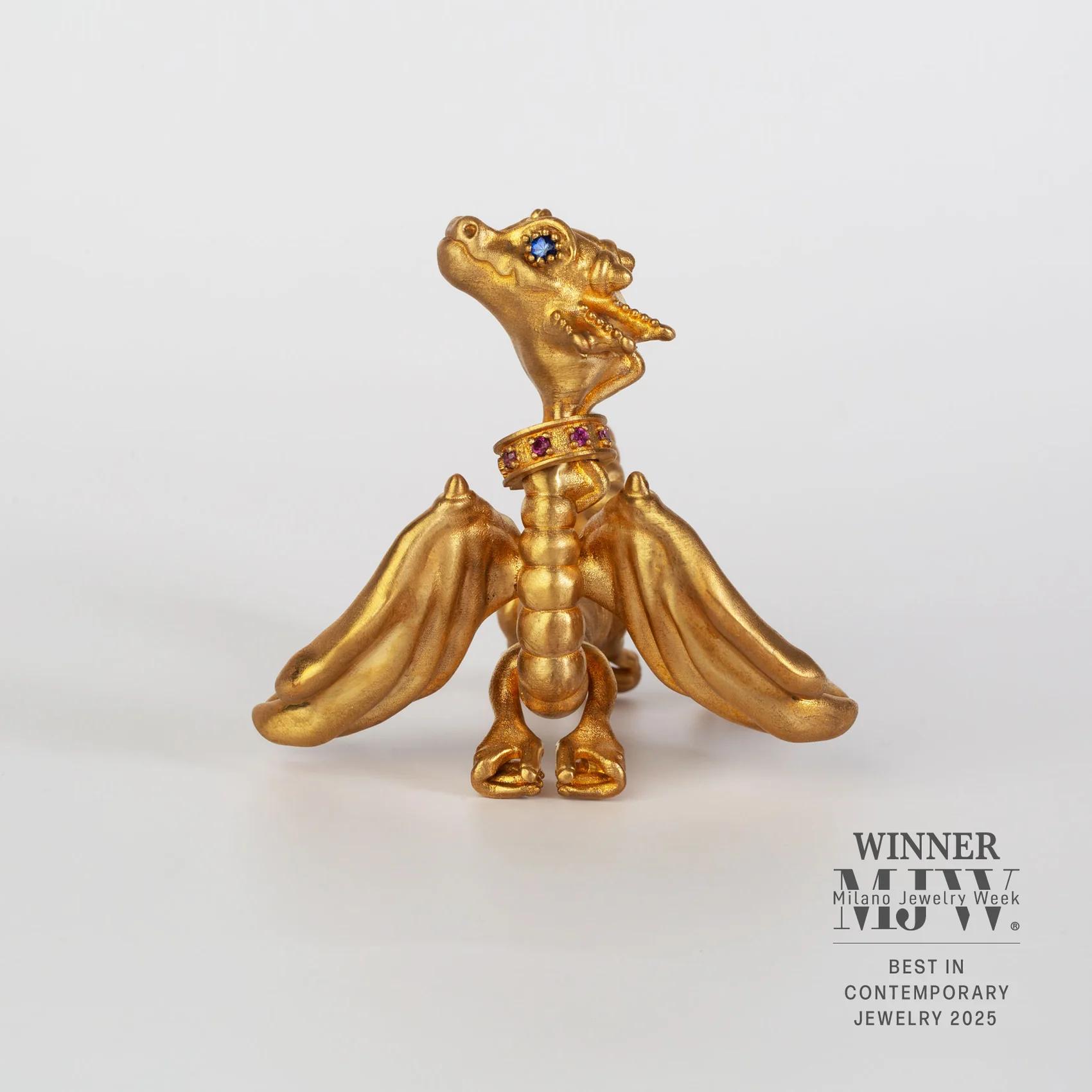 Freestanding gold-vermeil dragon shoulder jewel with broad sculpted wings, blue gemstone eyes and a red gemstone collar on a white background.
