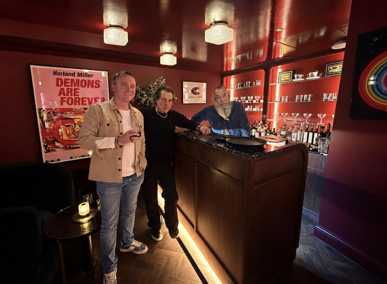 Andrew Martyniuk, Stephen Webster and Nick Strangeway standing together at the bar inside the red-walled No Regrets Lounge in London