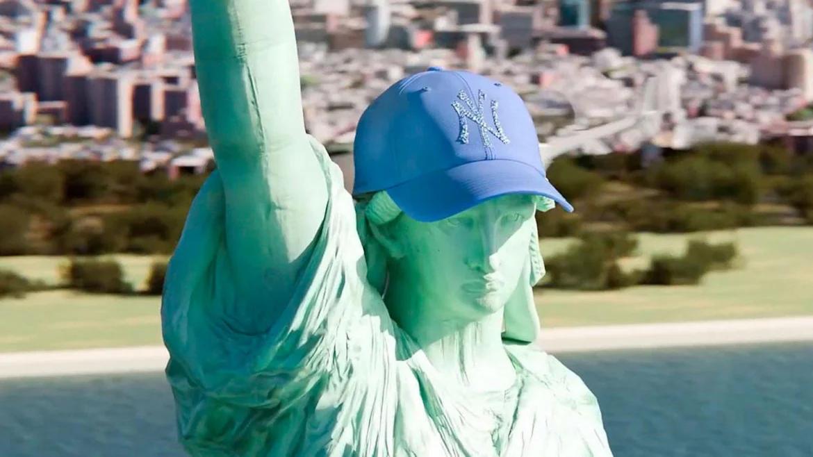 The Statue of Liberty wearing a blue New York Yankees baseball cap featuring a Swarovski crystal-covered NY logo, overlooking the New York skyline.