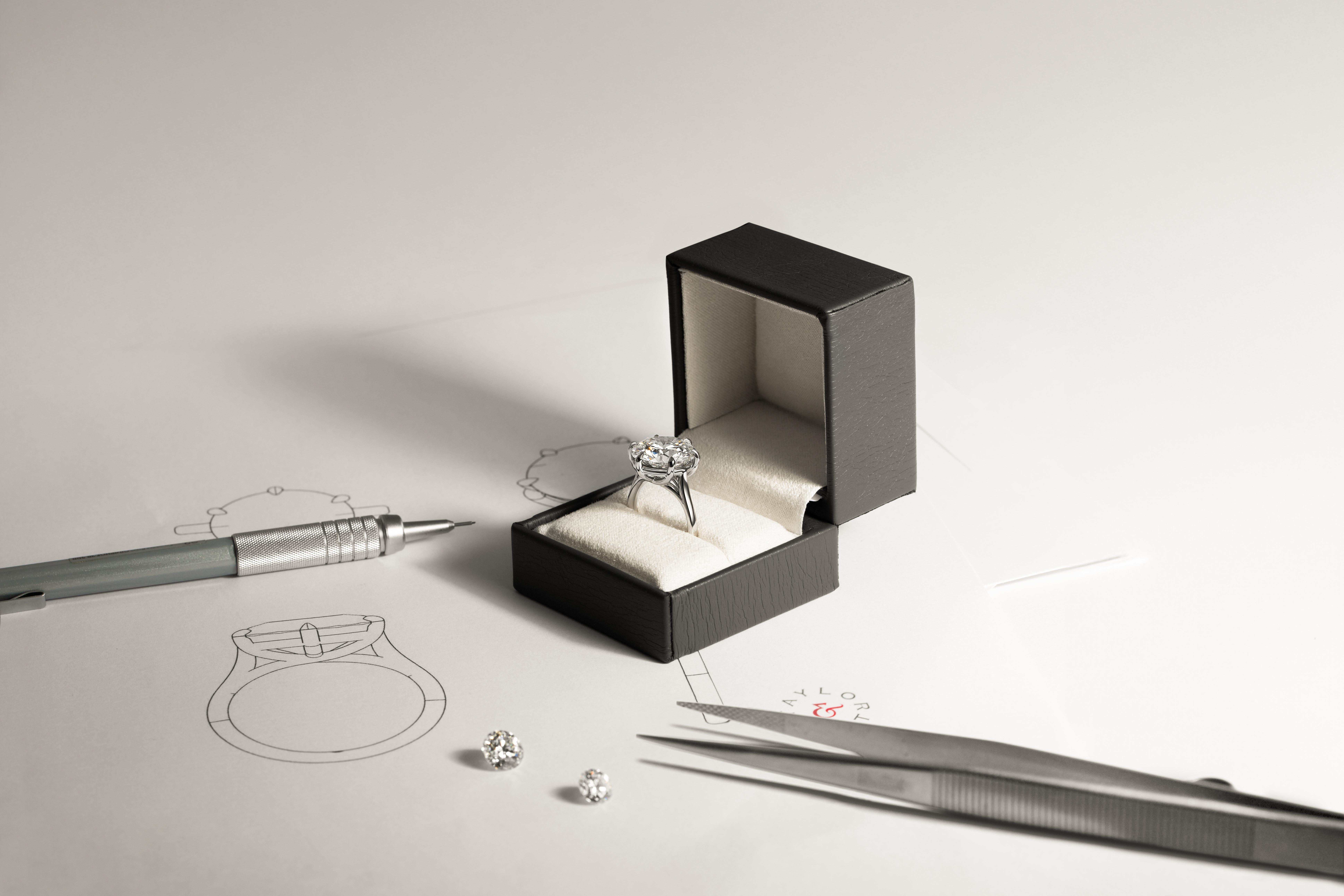 Engagement ring in a box with diamond sketches, loose stones and jewellery tools on a work surface