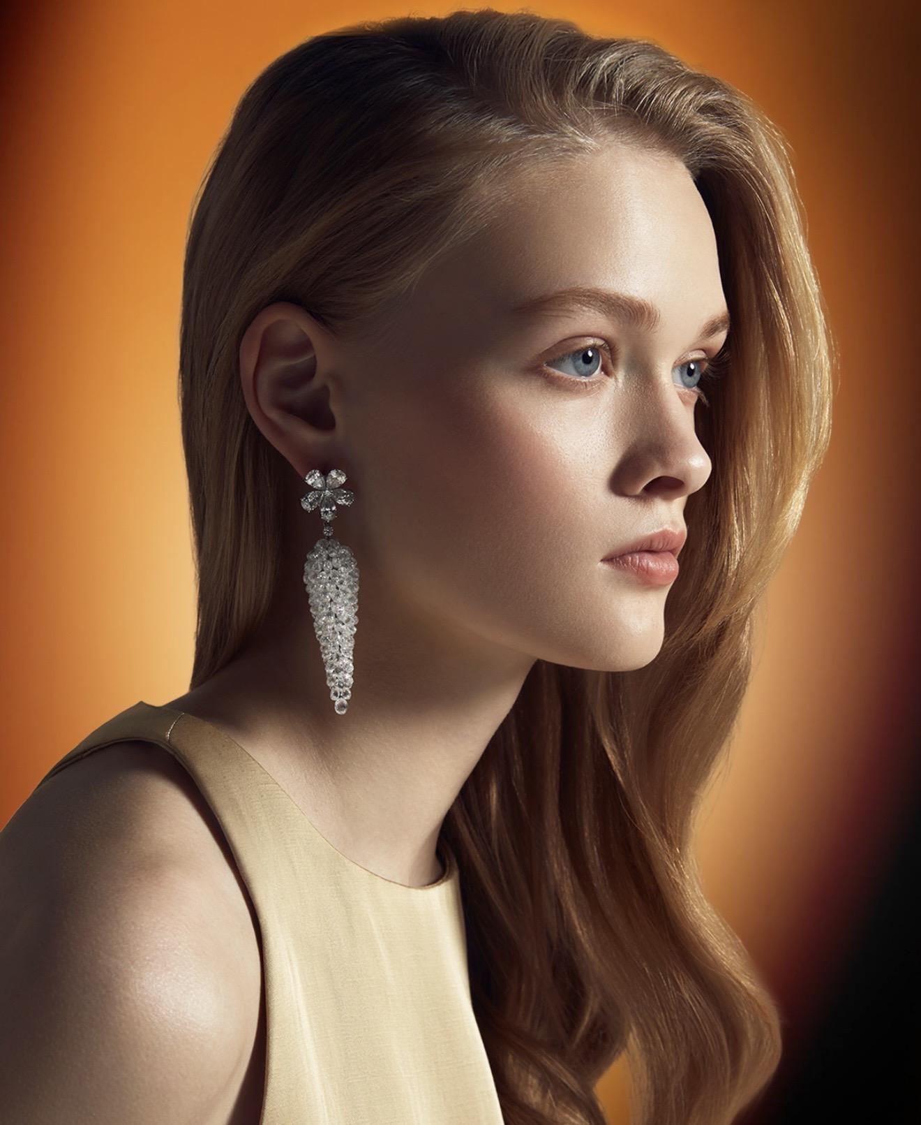 Model wearing 130.63-carat diamond drop earrings by Spitaleri Jewellers featuring briolette and pear-shaped diamonds against a warm orange background.