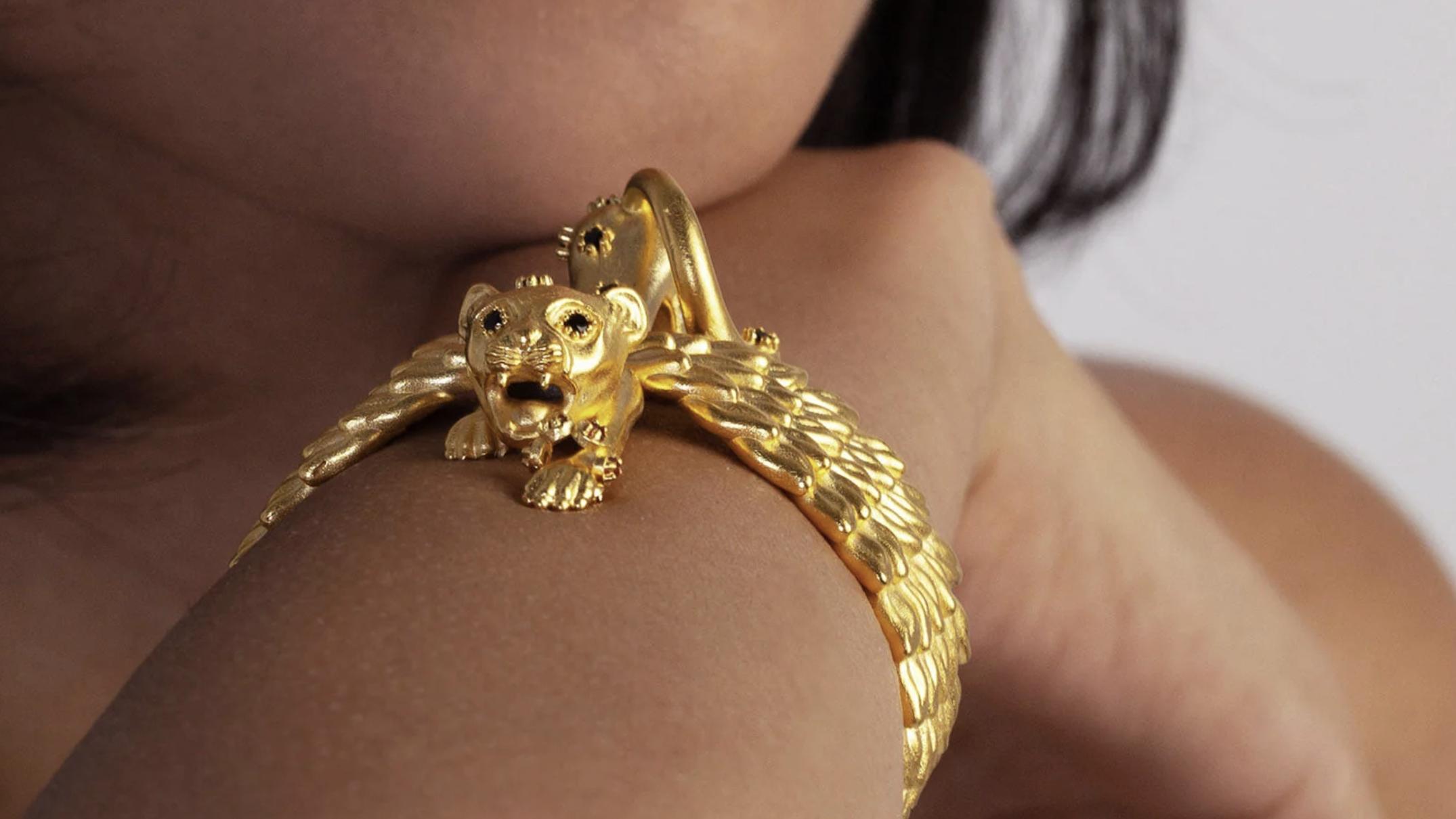 Close-up of a gold winged-cheetah jewel worn across a model’s shoulder, with black gemstone details on its face.