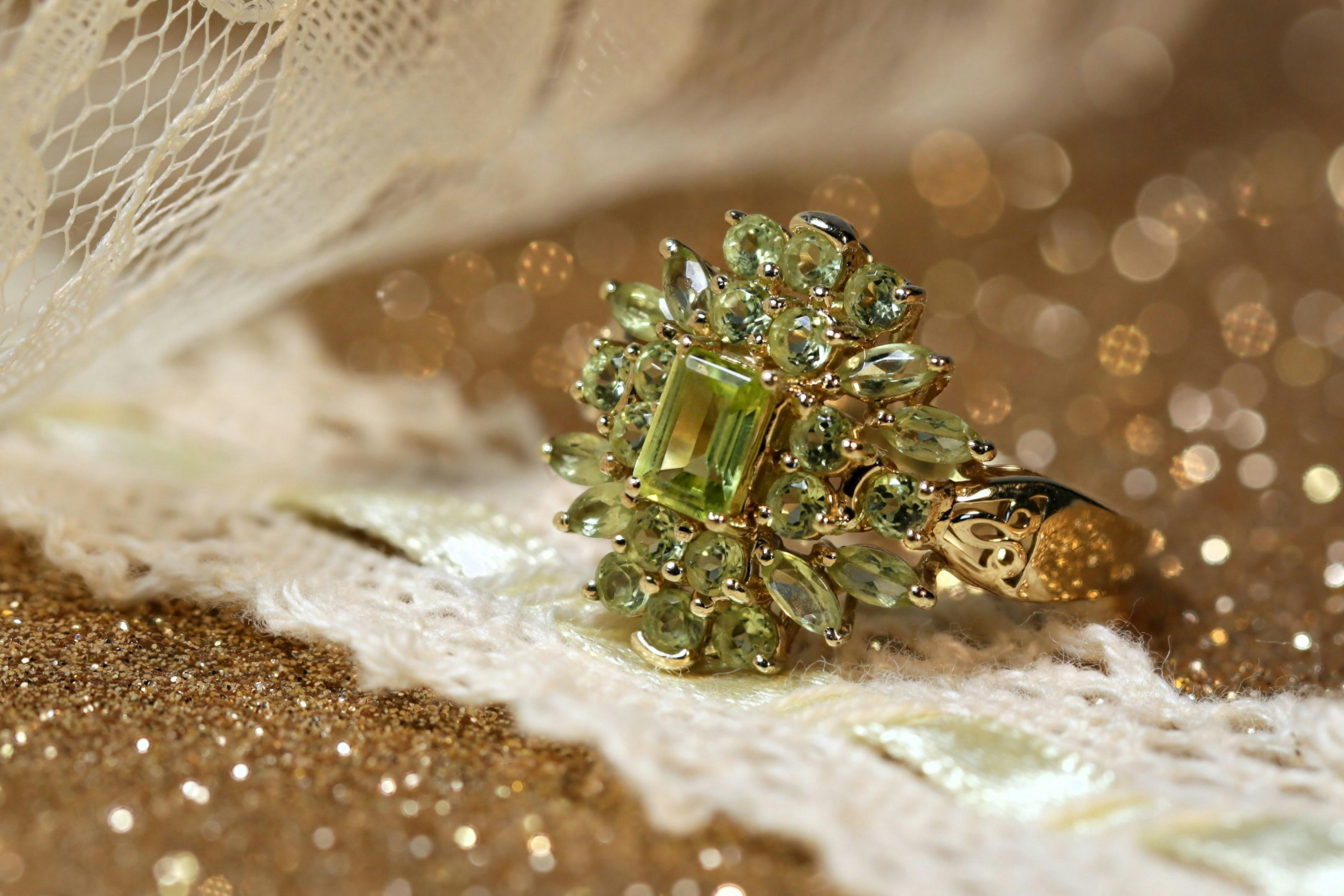 Ornate gold cocktail ring featuring an emerald-cut pale green centre stone surrounded by round and marquise-cut green gemstones.