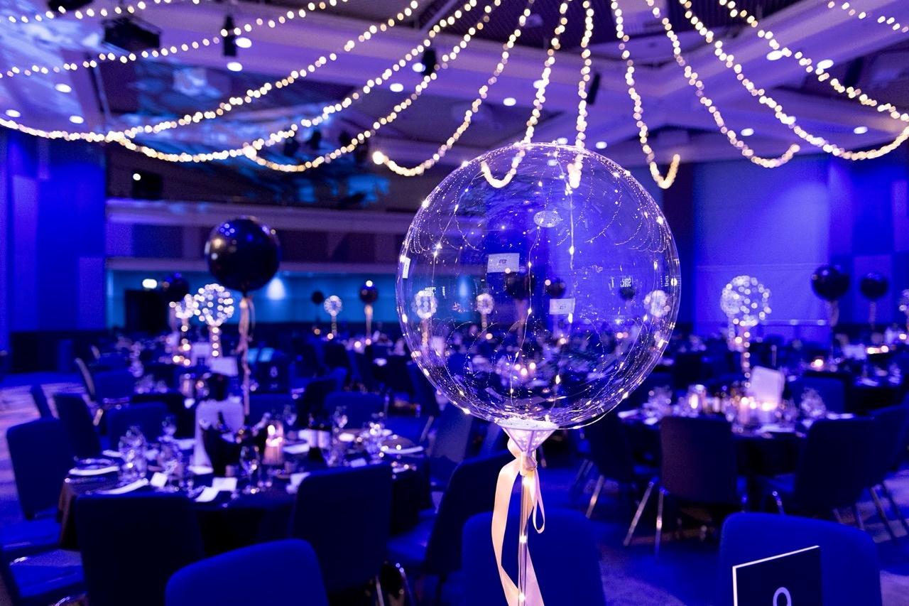 Decorated awards dinner venue at the International Convention Centre in Birmingham, with round tables, blue lighting and illuminated ceiling decorations.