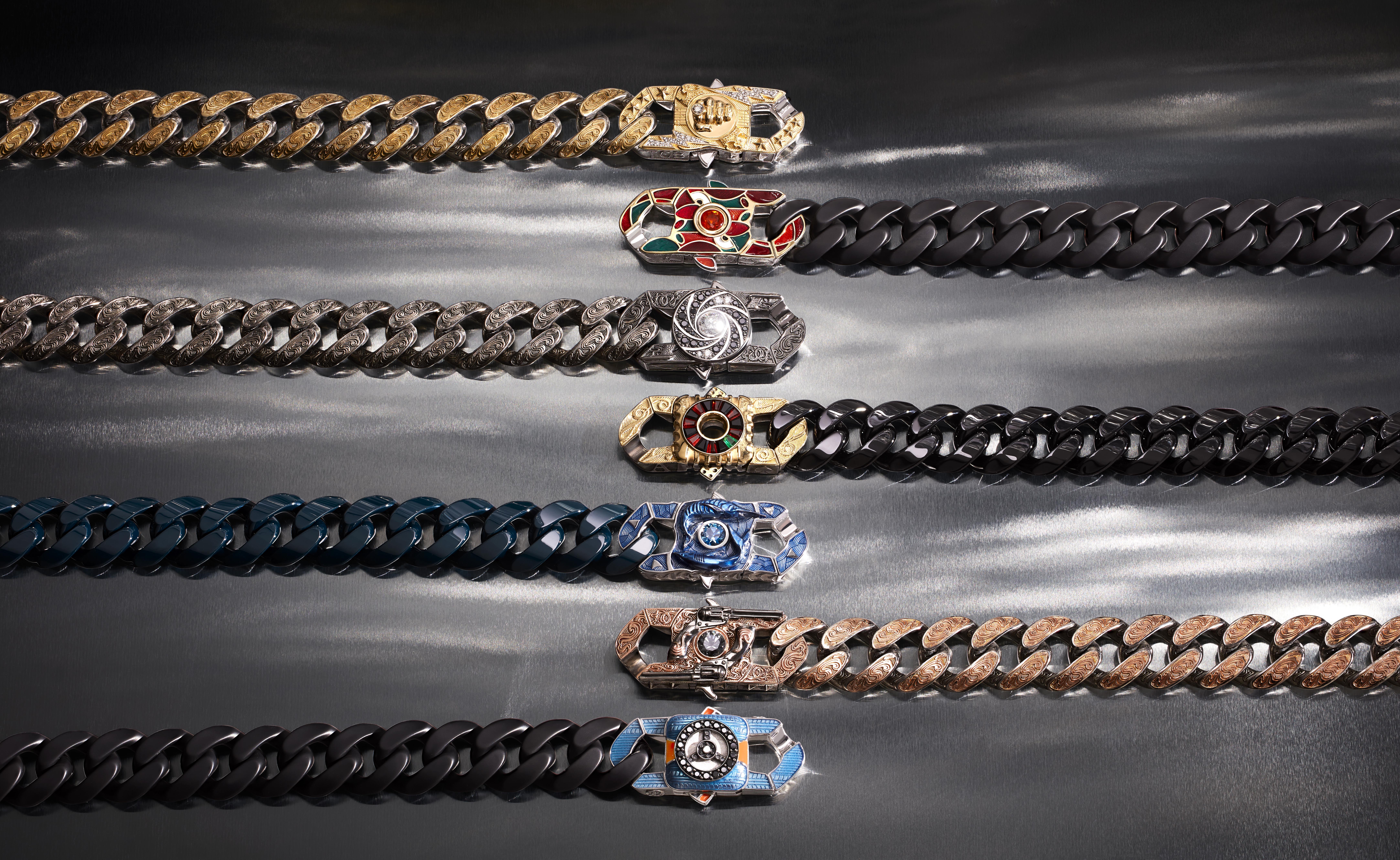 Seven Stephen Webster Magnificent Seven bracelets arranged on dark satin, featuring engraved metal and coloured ceramic Cuban links with gemstone-set clasps.