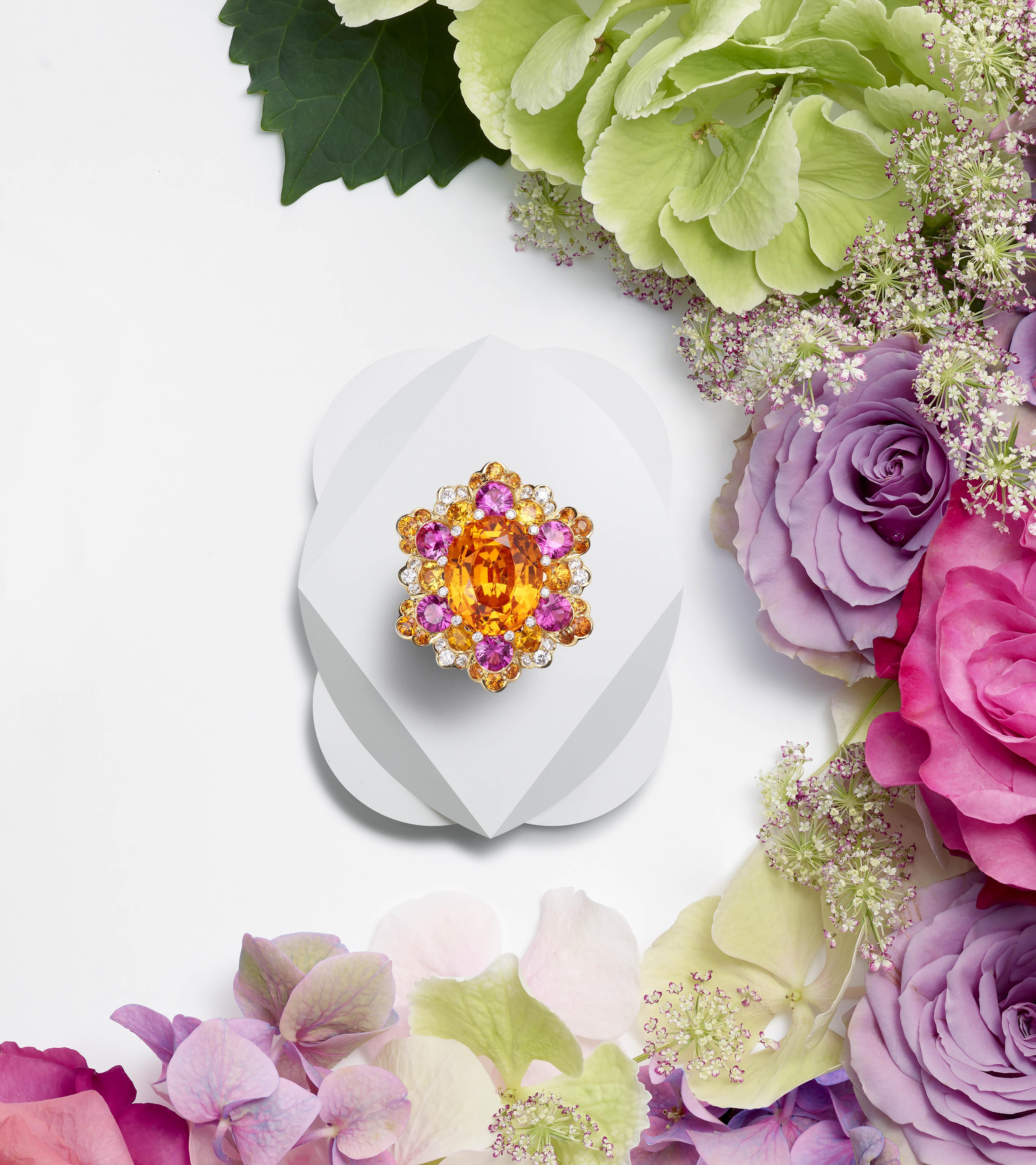Gold ring with oval mandarin garnet surrounded by pink and orange sapphires, spessartine garnets and diamonds on a floral background