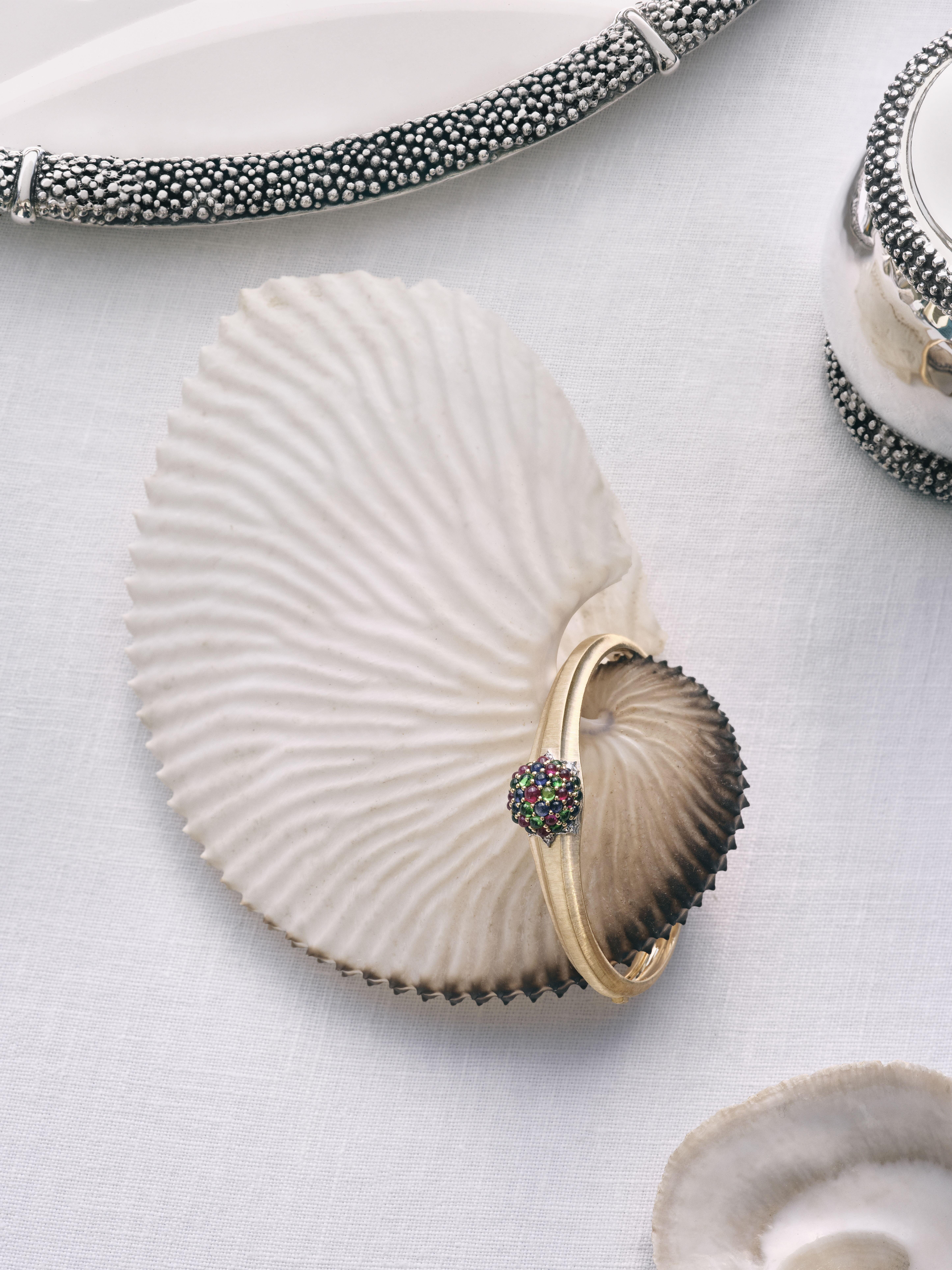 Buccellati Muse collection bracelet with rubies, sapphires and tsavorites displayed on a shell-inspired prop beside silver Caviar motif jewellery.
