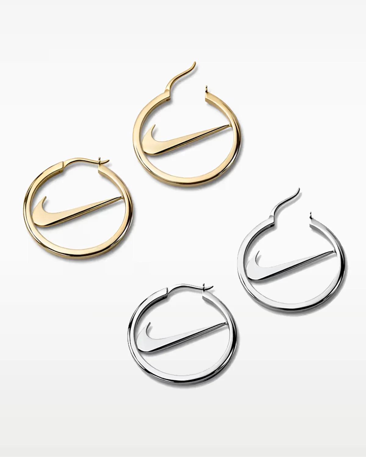 Two pairs of circular Nike hoop earrings in gold and silver finishes, each with a Swoosh spanning the open centre