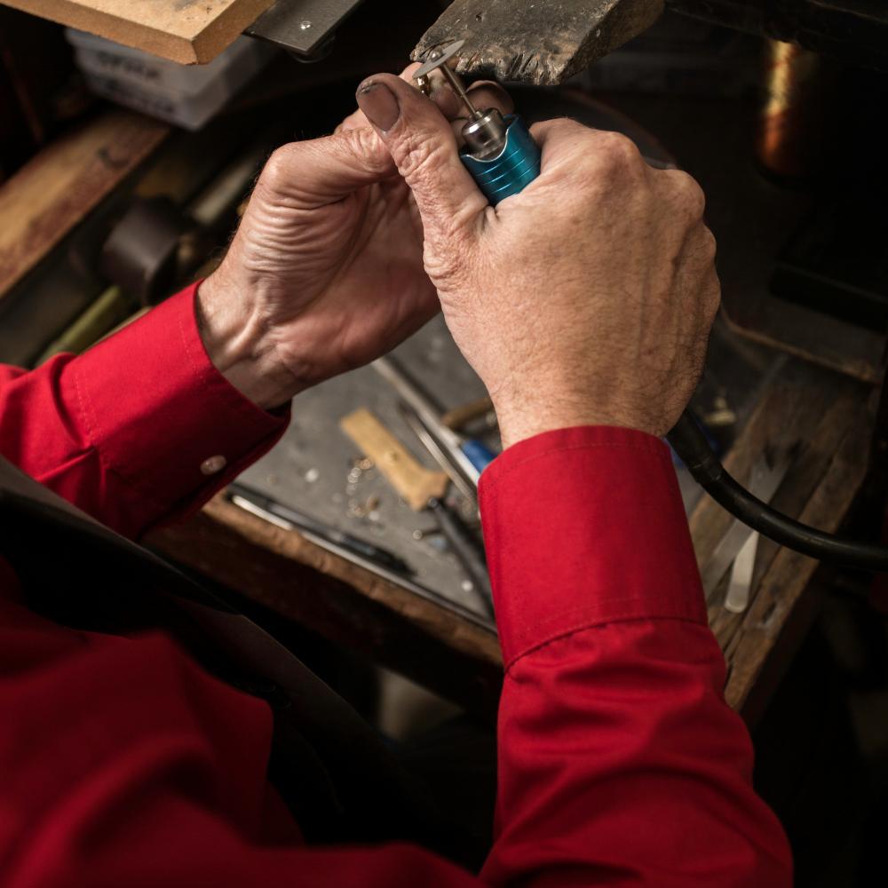 Close-up of a jeweller in a red shirt using a rotary tool to work on a small piece at the bench