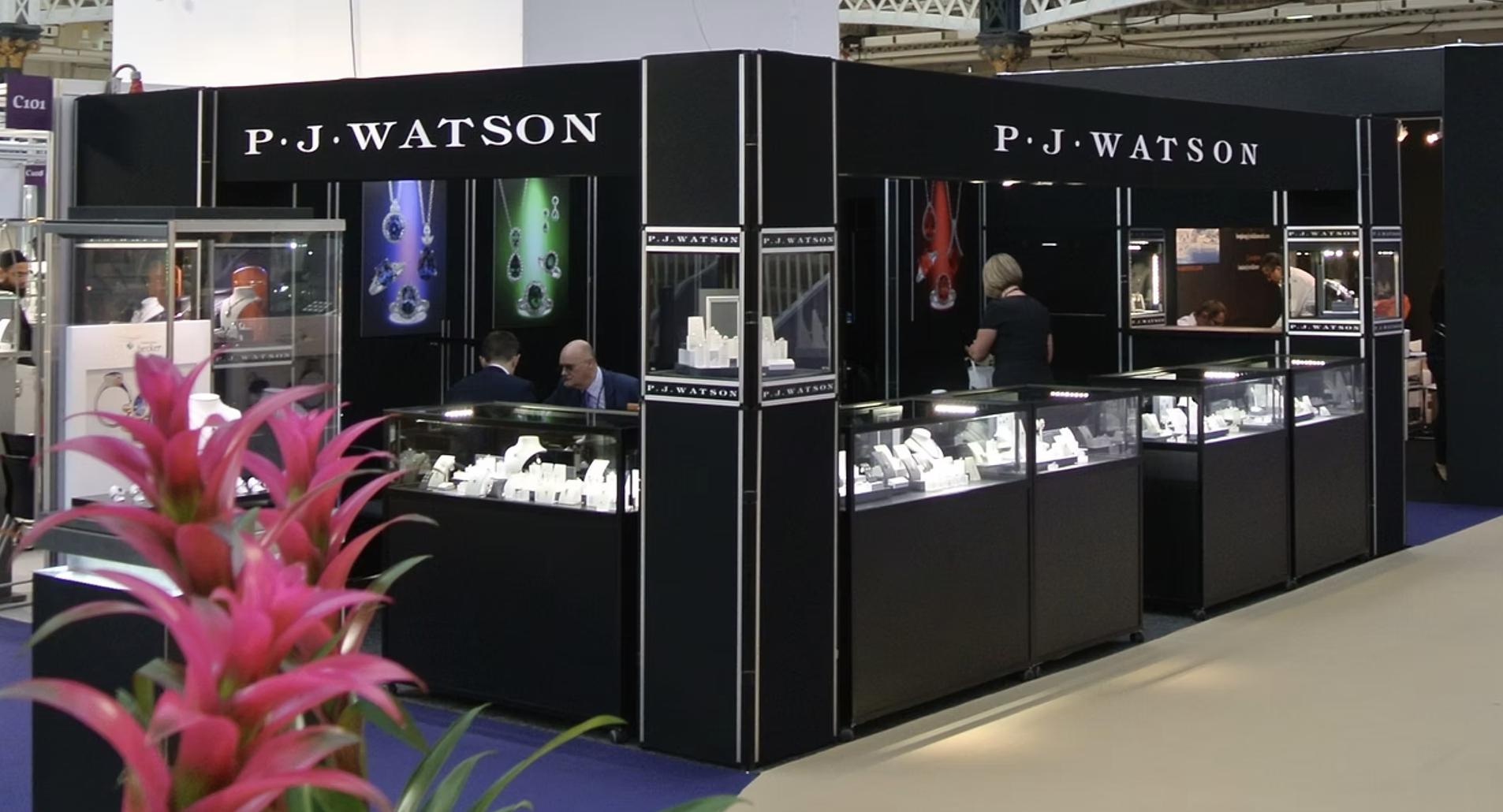 PJ Watson&rsquo;s black exhibition stand at The Jewellery Show London, with illuminated jewellery display cabinets and gemstone campaign imagery