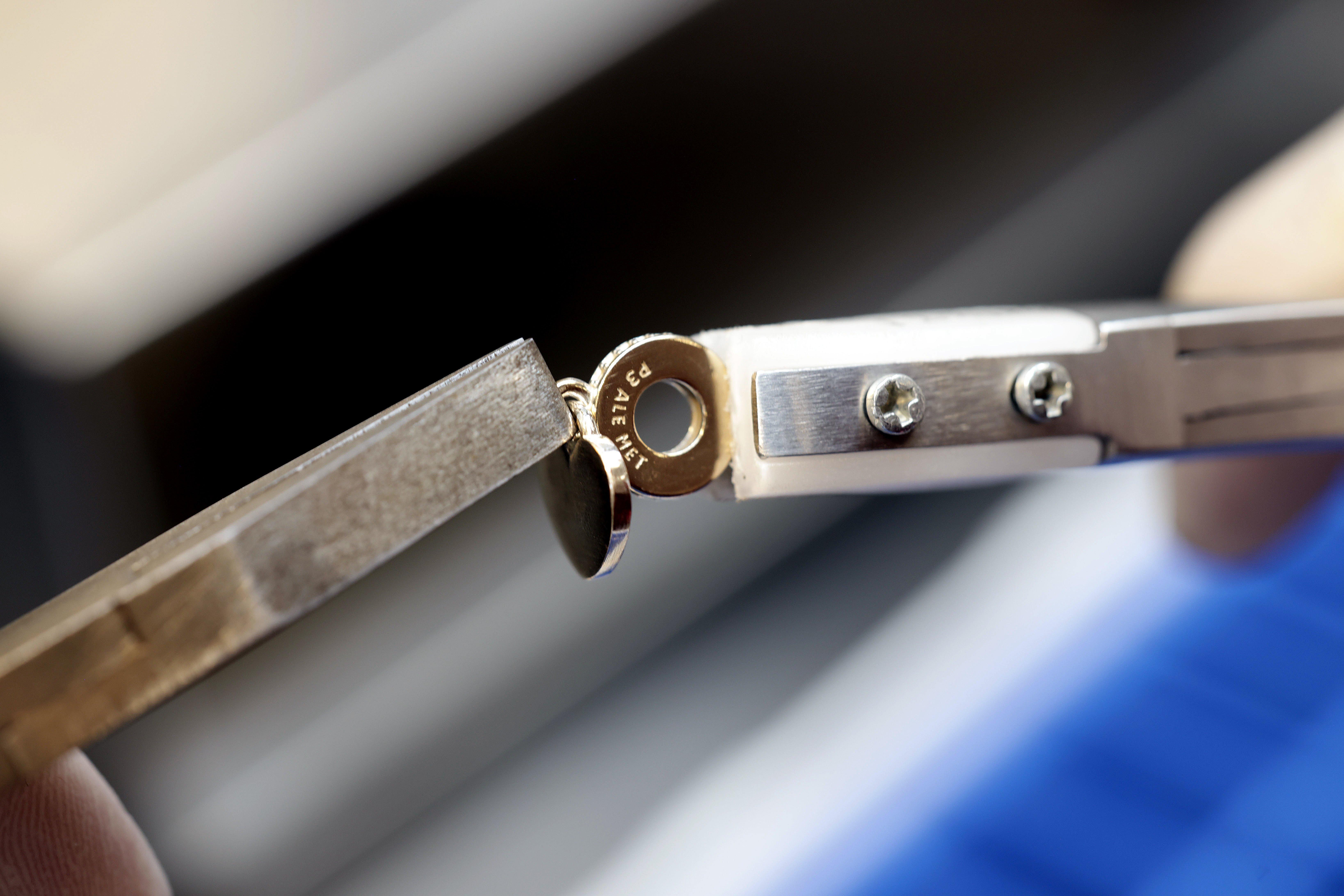 Close-up of a craftsperson using two precision tools to assemble small gold-coloured Pandora charm components.