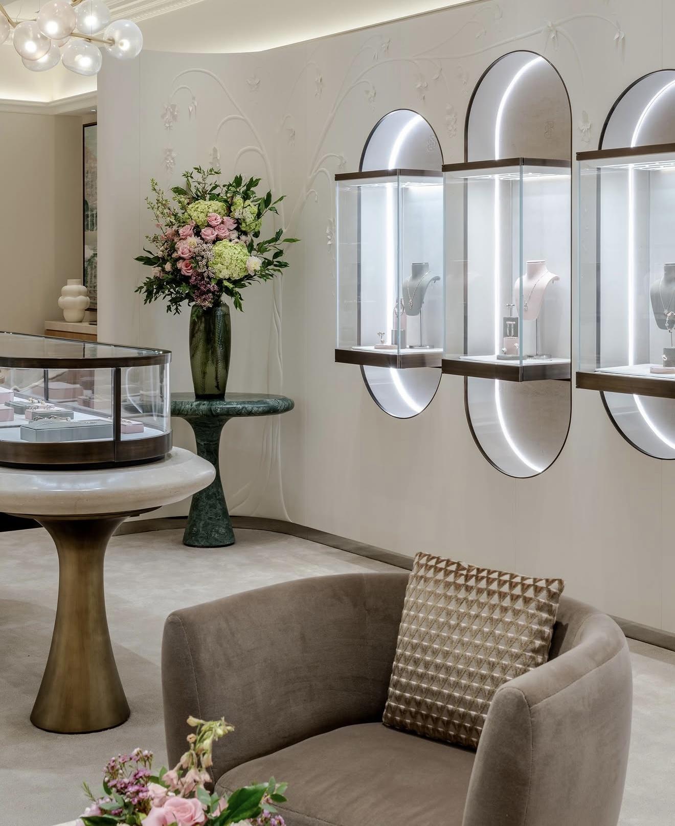 Interior of The Boodles Townhouse with illuminated jewellery cabinets, a curved glass display case, neutral seating and arrangements of pink and green flowers