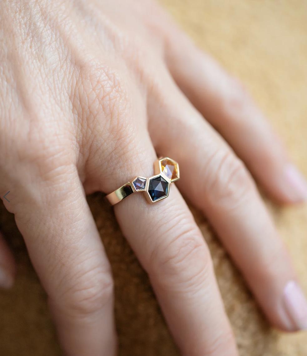 Mociun Spraybow gold ring with three geometric sapphires in blue, violet and golden yellow, worn on a hand