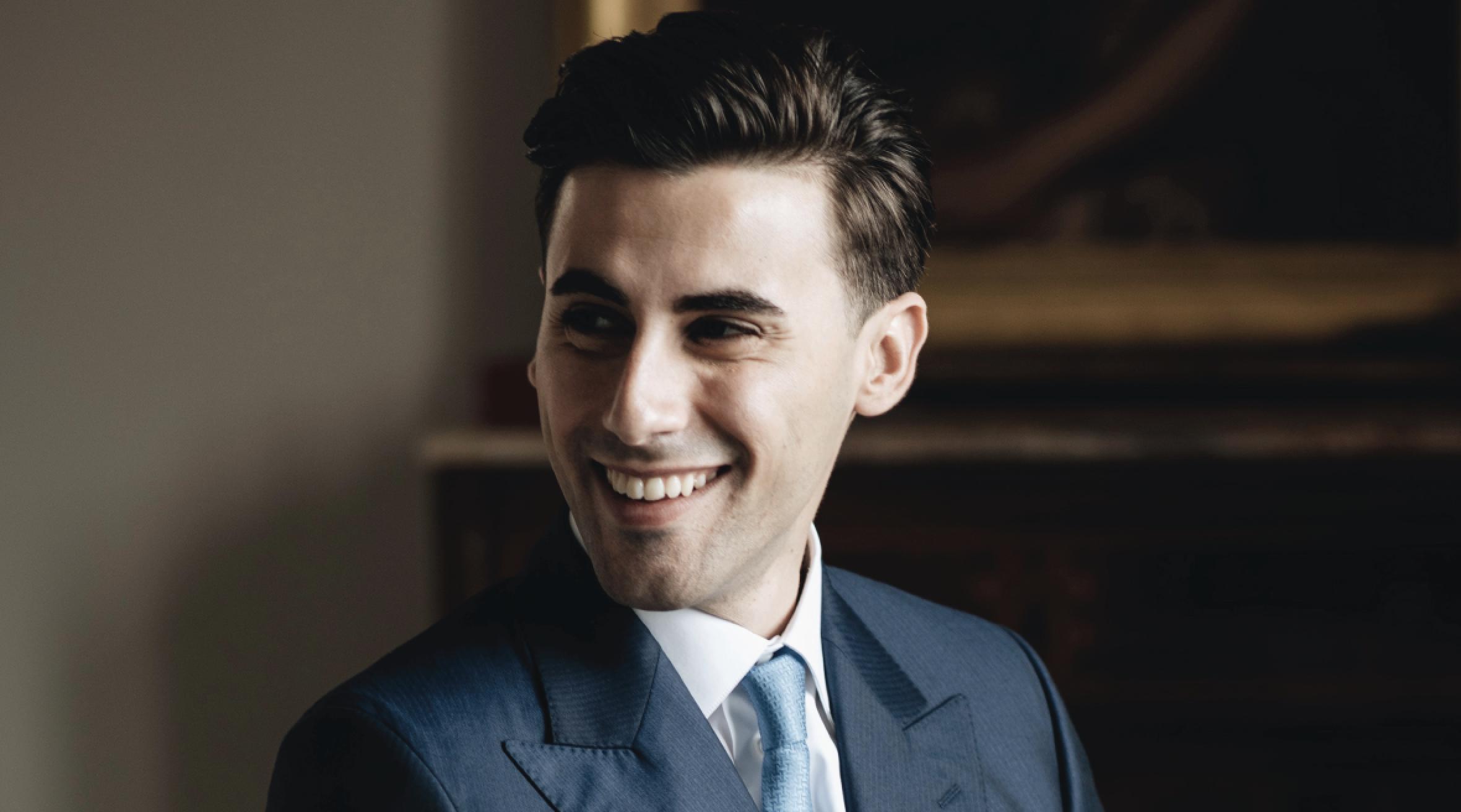 Portrait of Giovanni Prigigallo, Co-Founder of EveryWatch, wearing a blue suit and light blue tie, smiling during an interview setting.