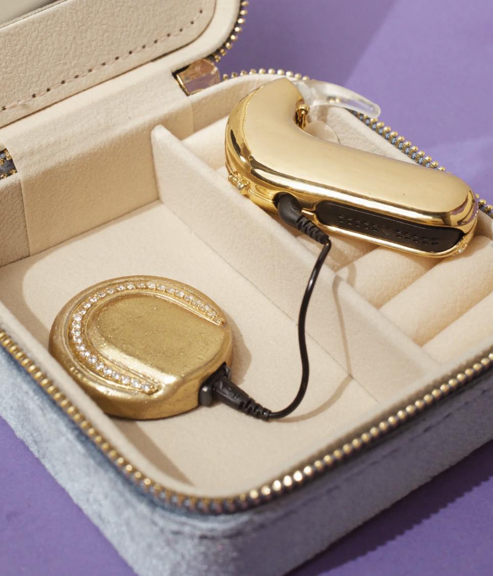 Gold AUZI cochlear-implant processor and diamond-set coil covers connected inside a cream jewellery case