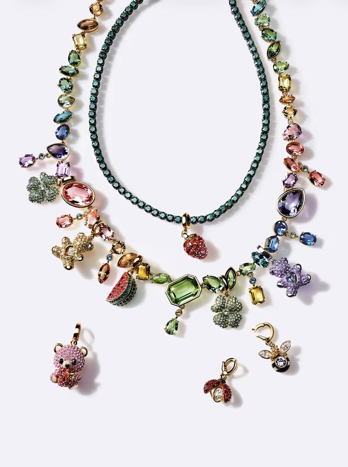 A Swarovski Idyllia necklace featuring multicoloured crystals and decorative charms, including strawberries, flowers, a teddy bear, a watermelon slice, a bee and a ladybird, presented against a light background.