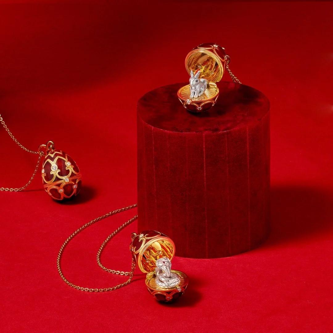 Faberg&eacute; Heritage egg pendants in red enamel and gold, opened to reveal miniature figures inside on a red background