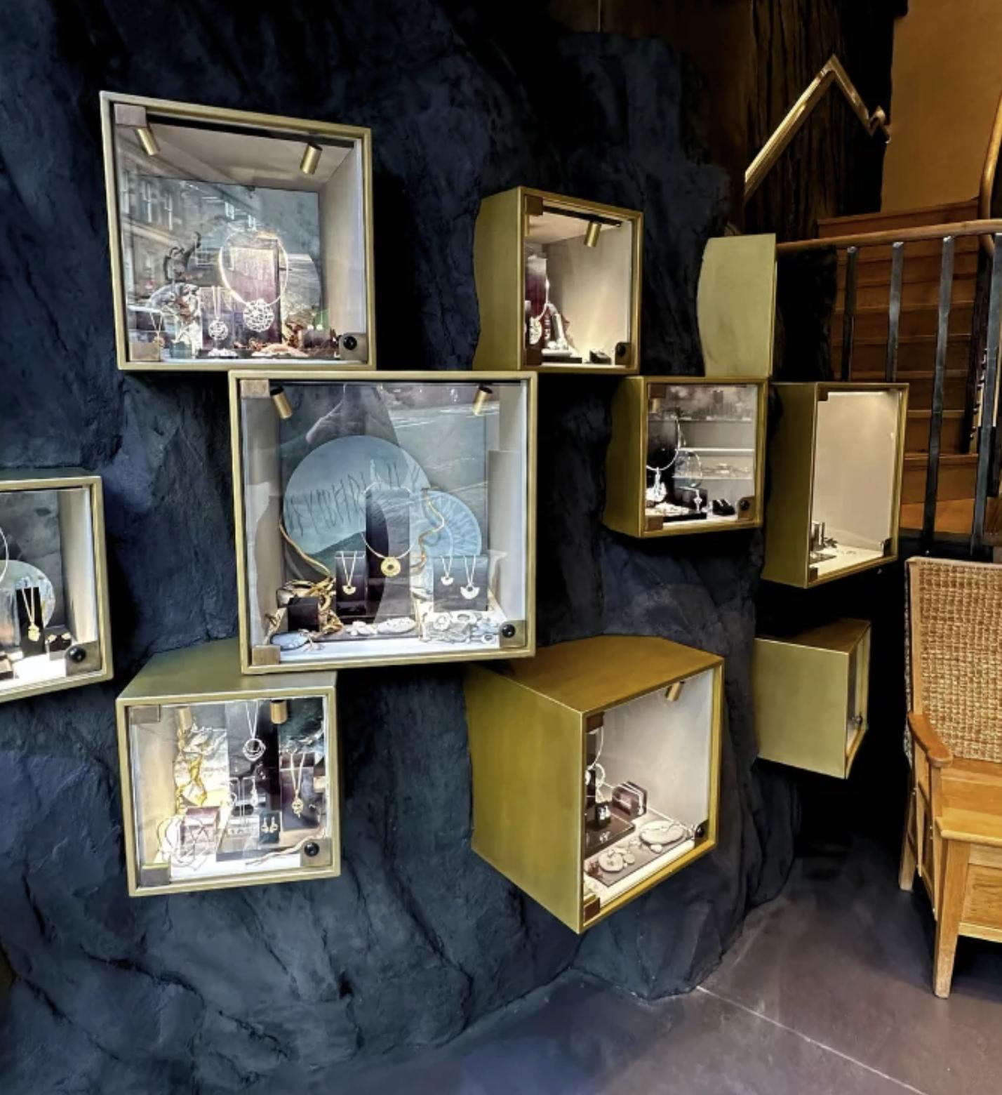 Illuminated gold jewellery cabinets set into a dark, textured rock wall inside Sheila Fleet Jewellery’s Hanover Street gallery