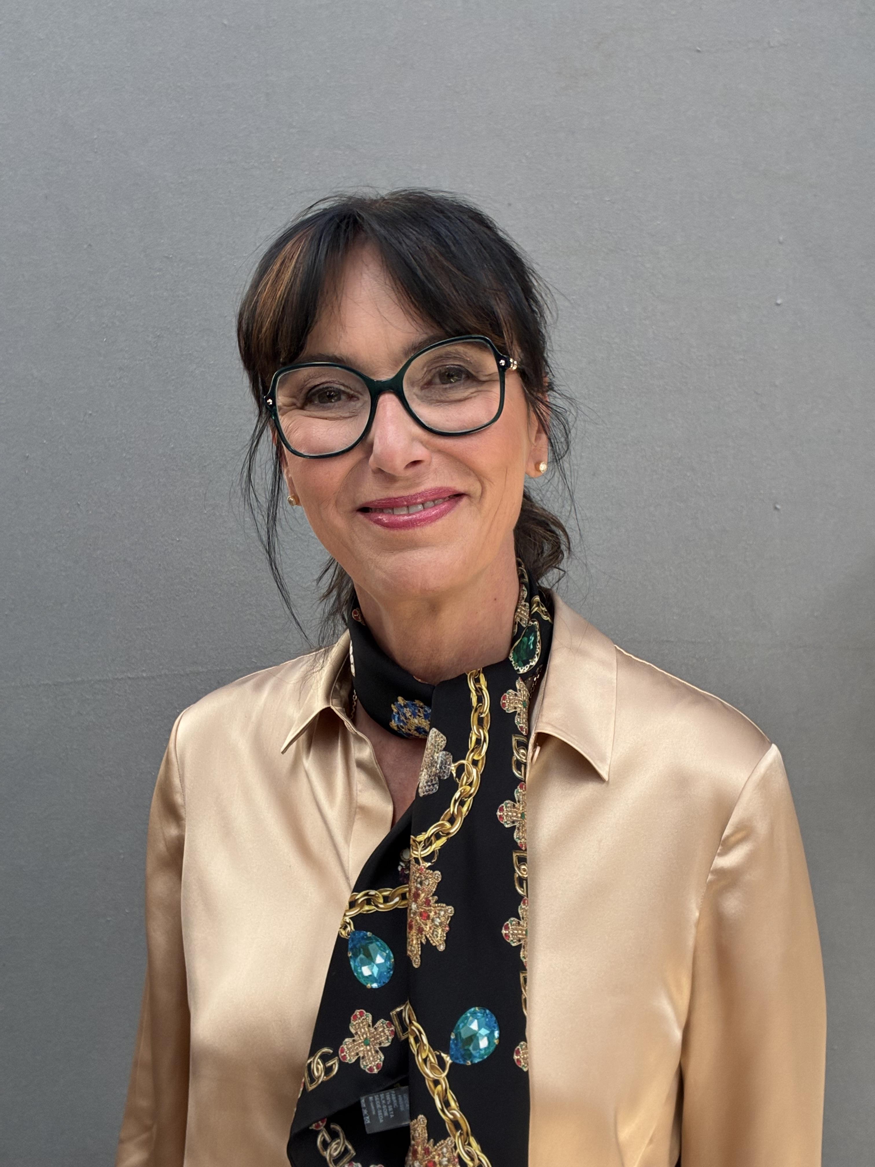 Portrait of Dr Heide Rezepa-Zabel wearing green-framed glasses, a champagne-coloured blouse and a black jewellery-print scarf