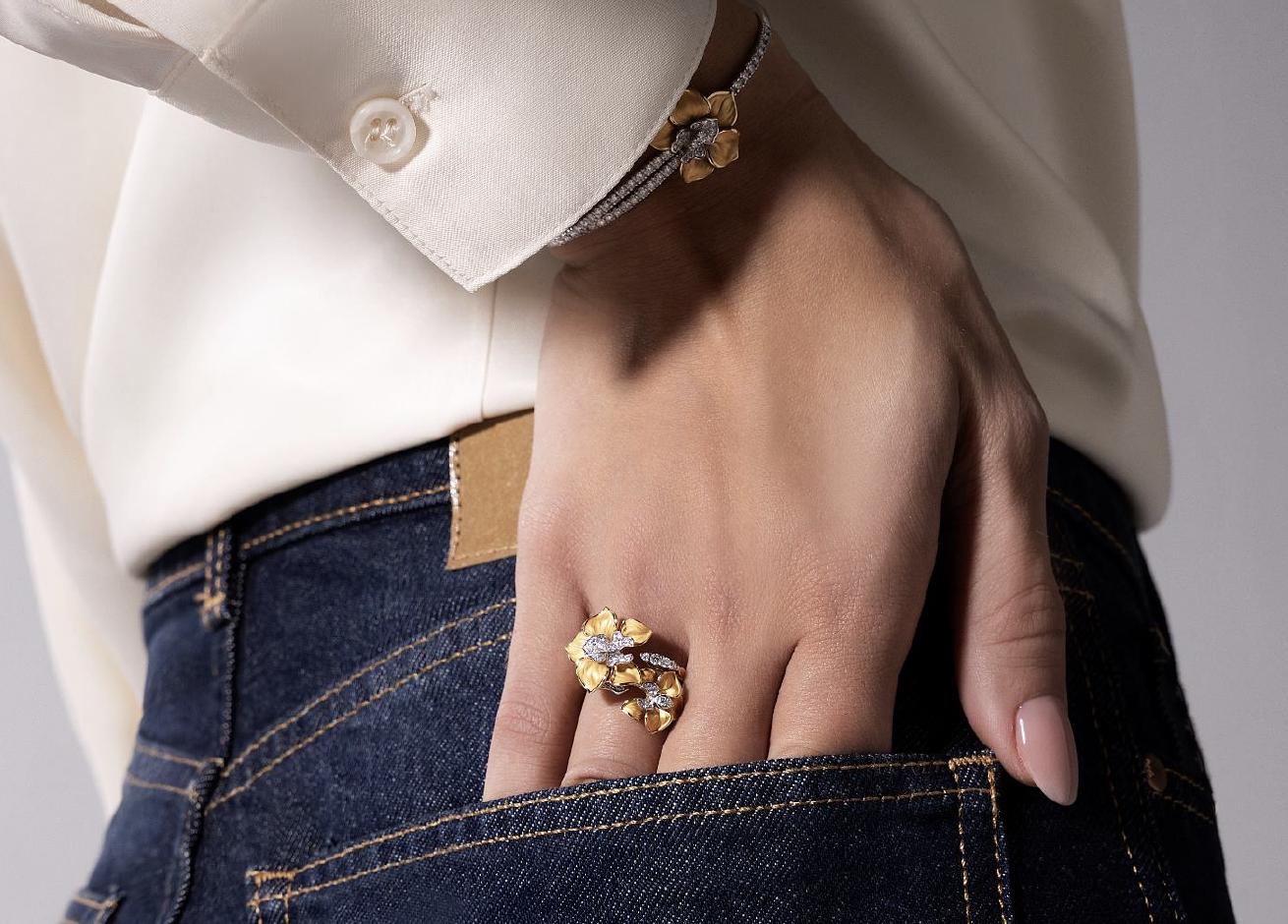 Close-up of a model wearing a yellow gold and diamond Orquídeas ring and matching bracelet with a white shirt and dark denim jeans.