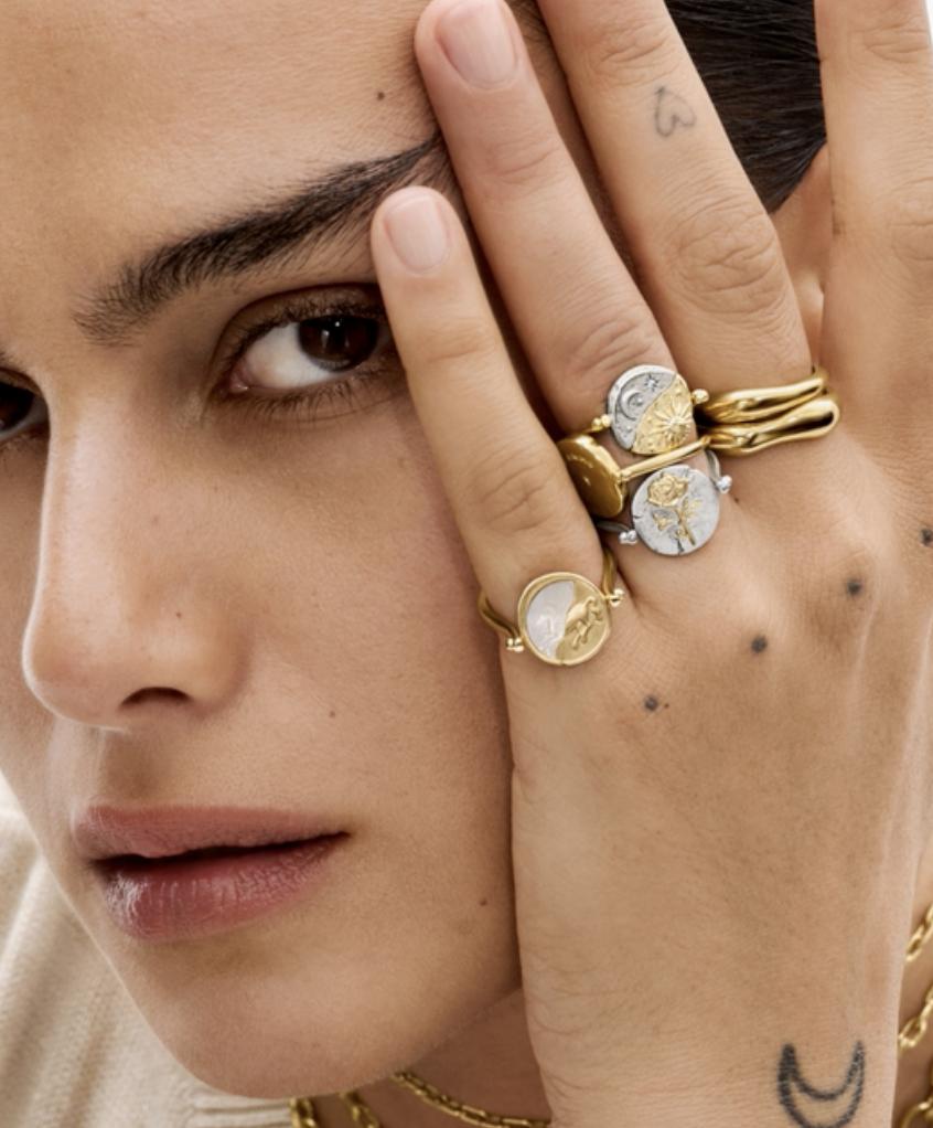 Close-up of a model wearing stacked gold and silver Pandora Talisman rings featuring celestial, floral and symbolic medallions