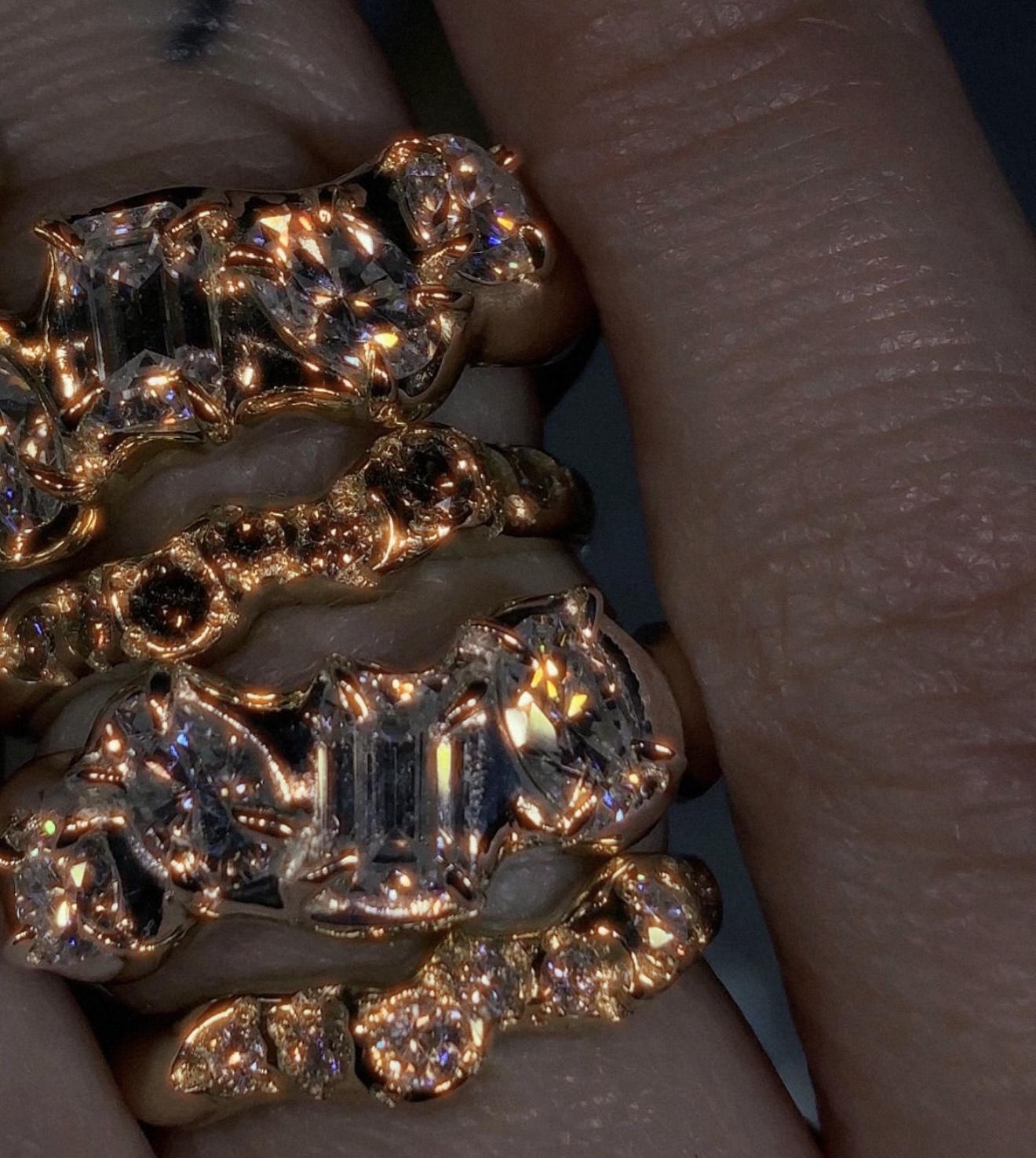 Close-up of several rose gold rings set with an assortment of faceted clear and dark gemstones, designed by Susannah King
