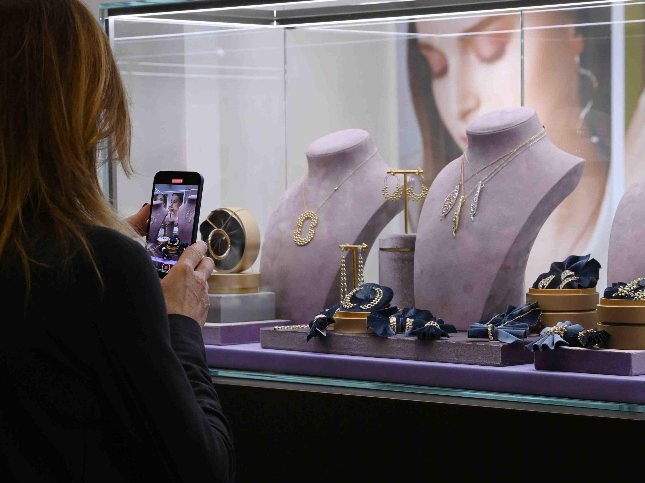Visitor photographing necklaces, earrings and bracelets displayed in a glass showcase at the Vicenzaoro jewellery trade show