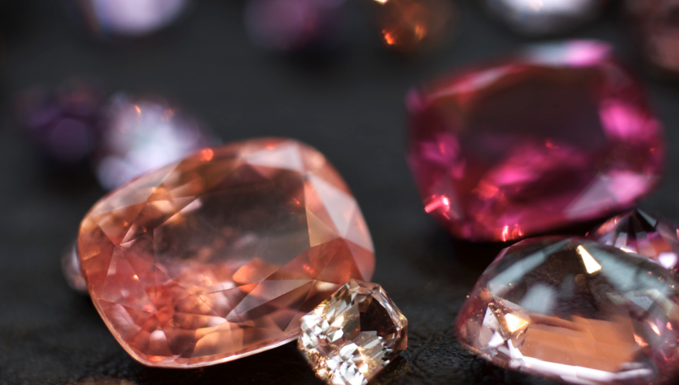 Close-up of vivid pink, peach, and lavender faceted gemstones from Wennick–Lefèvre, displayed on a dark textured surface.