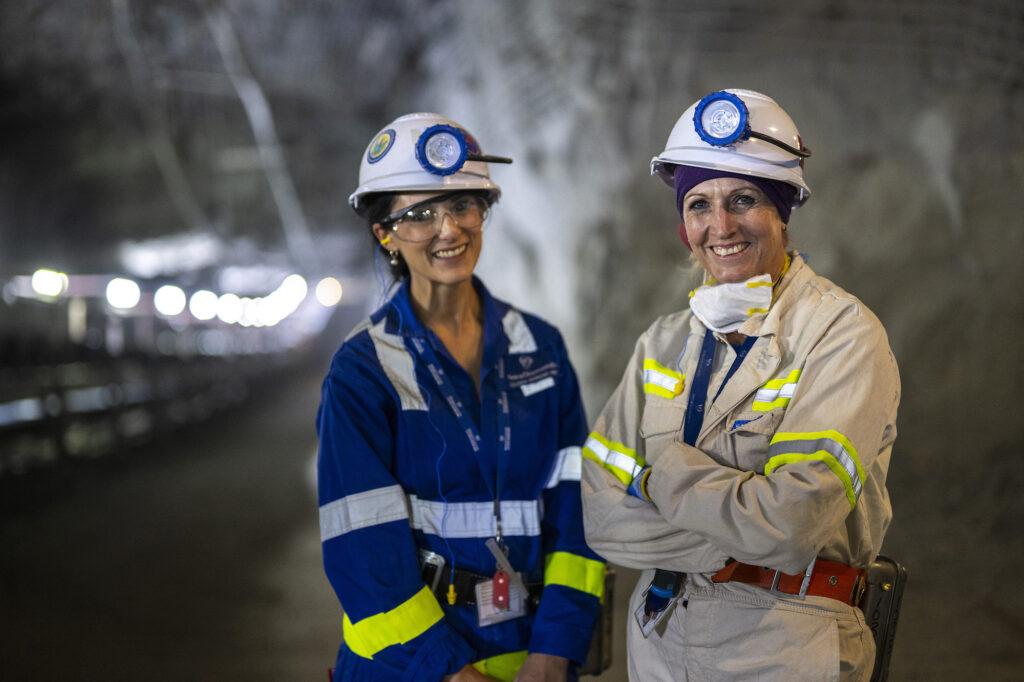 Two Petra Diamonds employees wearing helmets, headlamps and high-visibility protective clothing inside an underground mine.