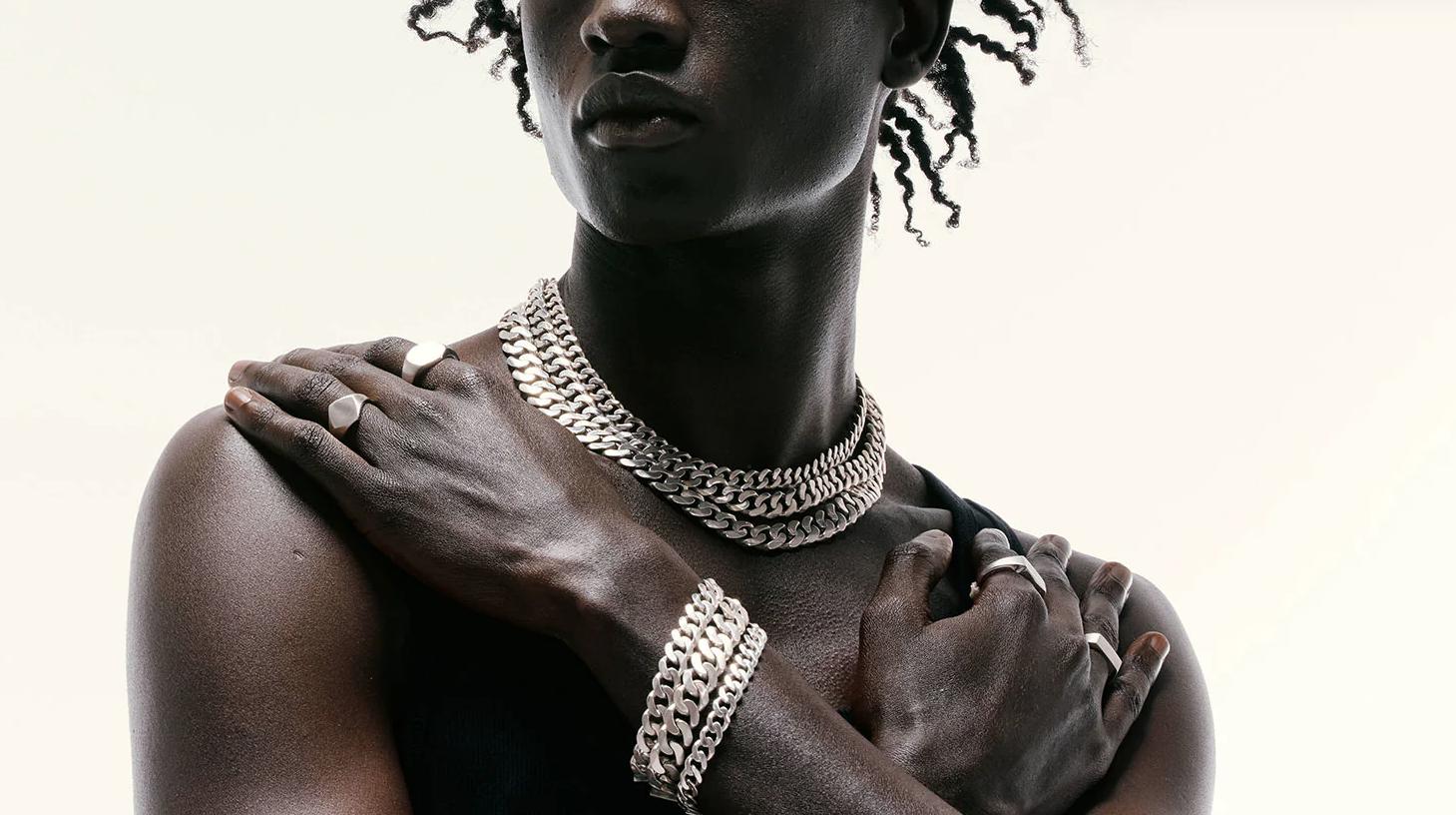 Model wearing layered silver chain necklaces, bracelets and rings from Serge Denimes against a neutral background.