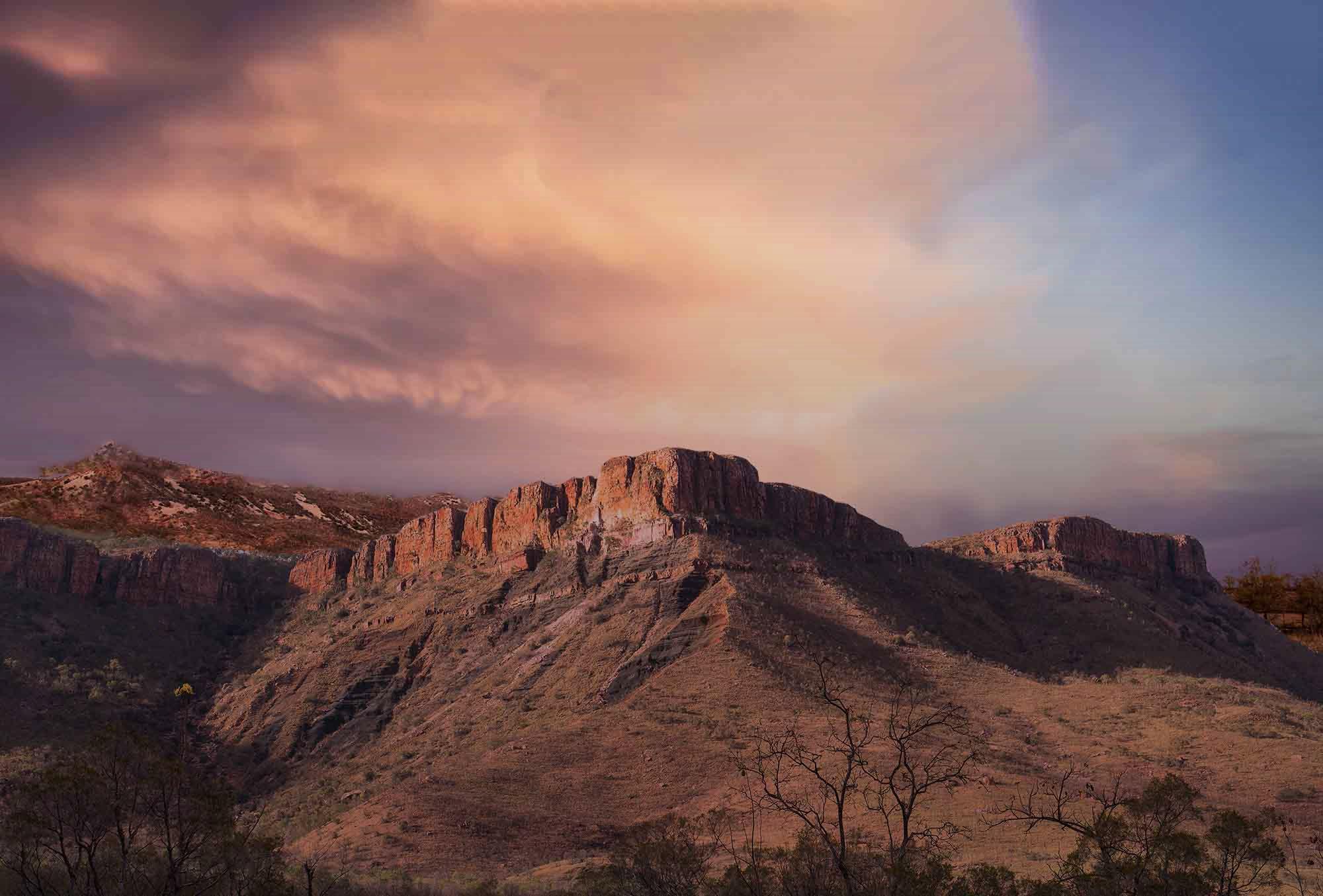 Sunlit red cliffs and rocky hills beneath pink and purple clouds in Western Australia’s East Kimberley region